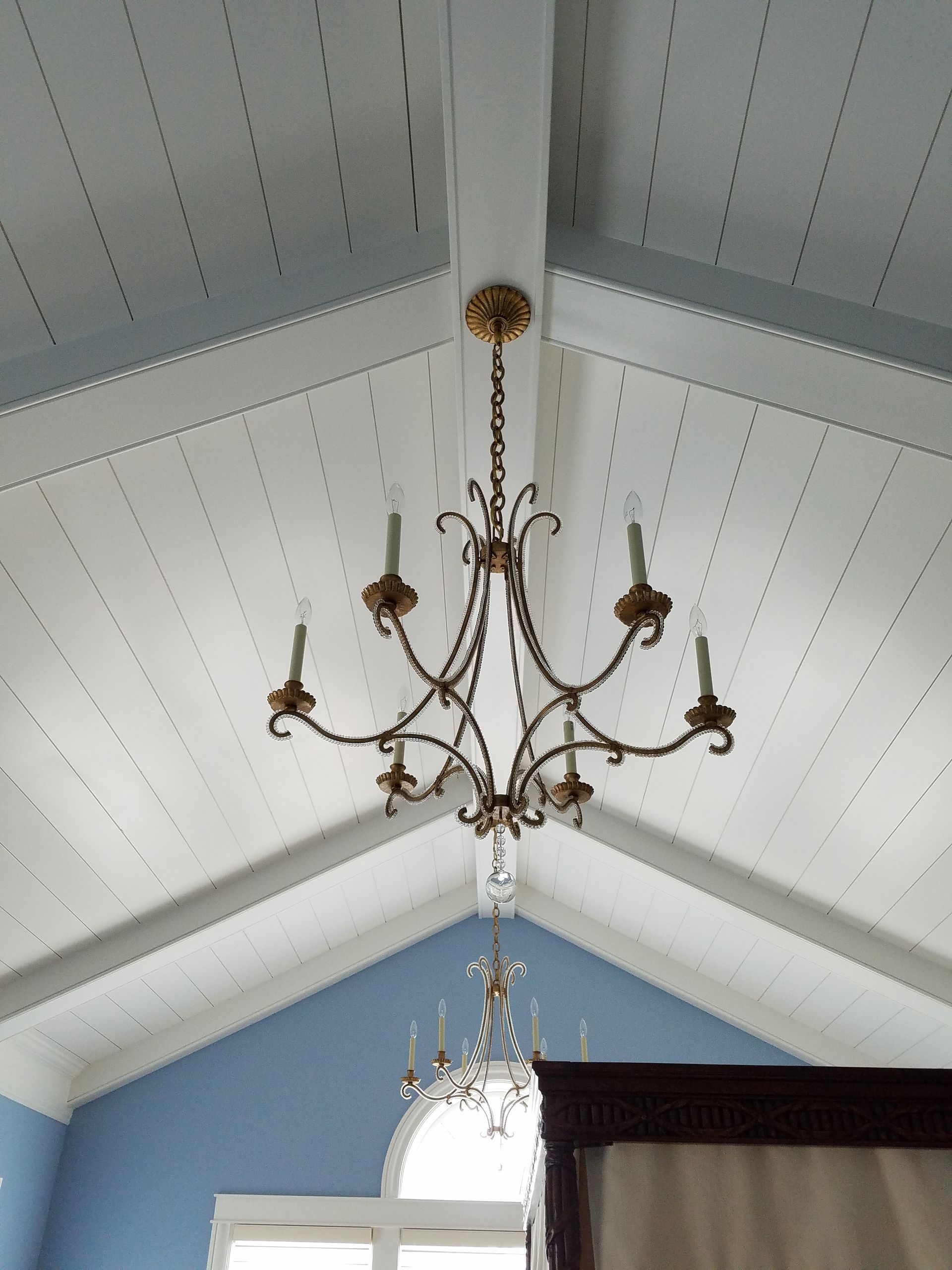 Chandelier hanging from a white slatted ceiling with blue walls.