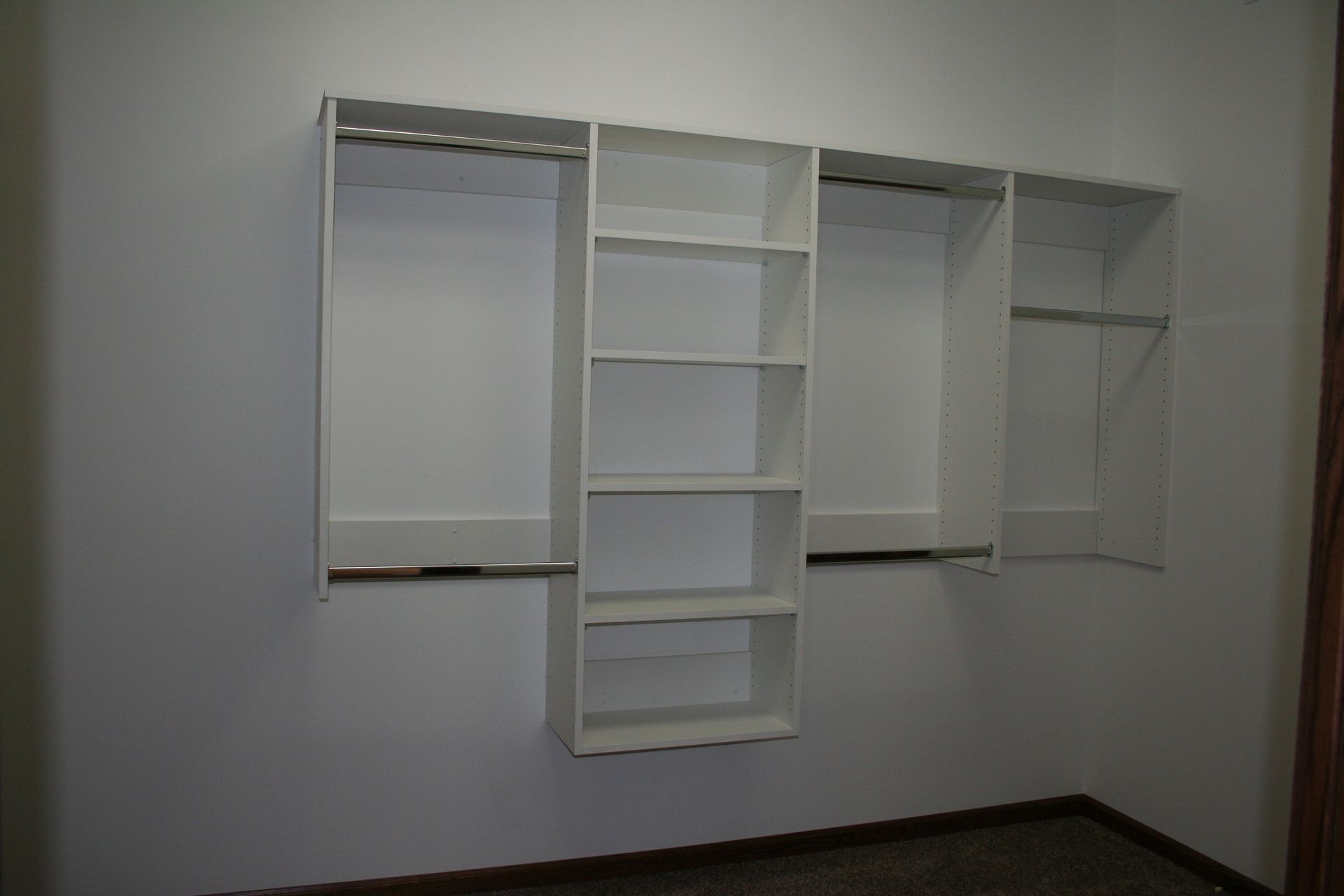 White closet organizer mounted on a white wall with shelves and hanging rods.