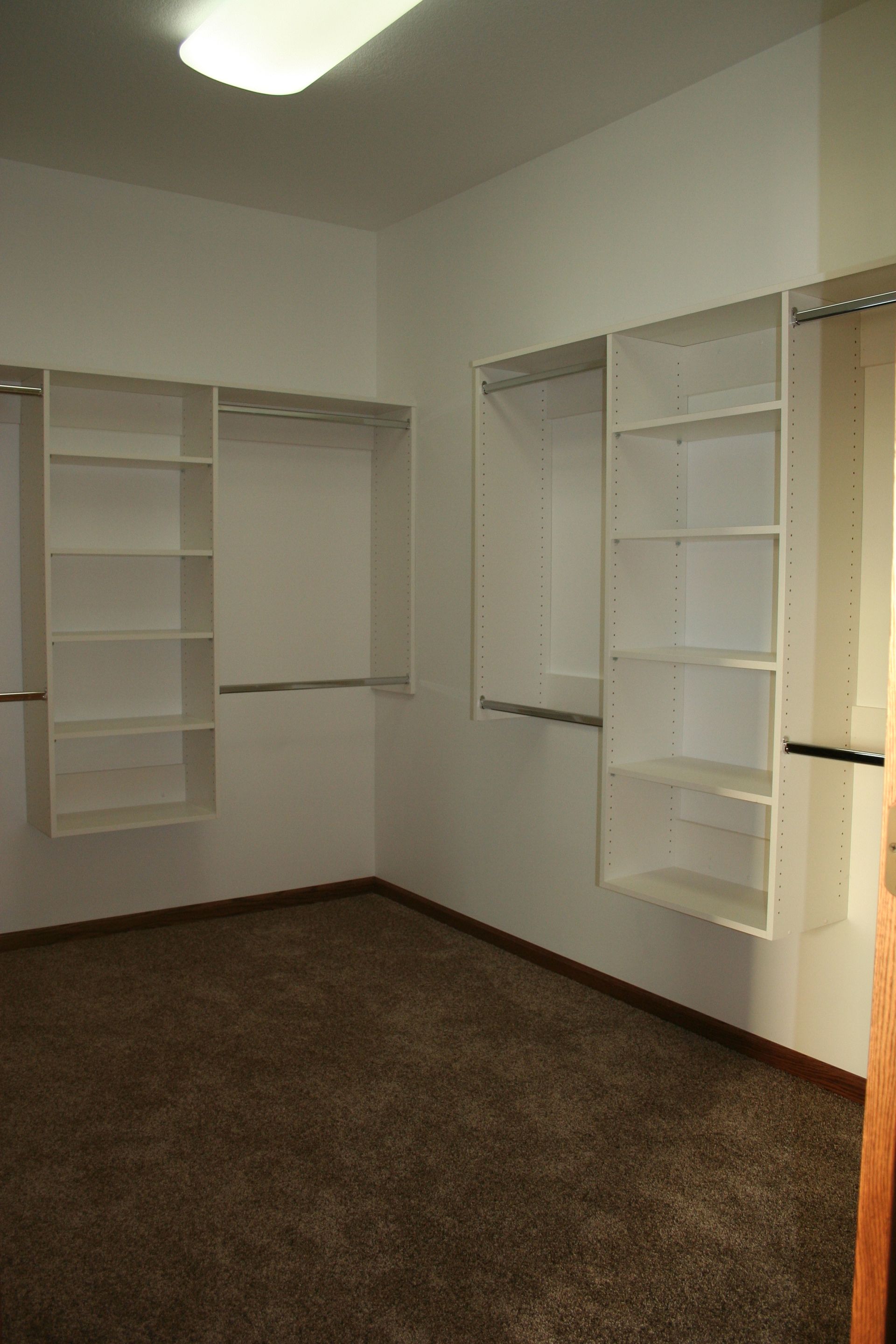 Empty white-walled closet with shelves, hanging rods, and brown carpet.