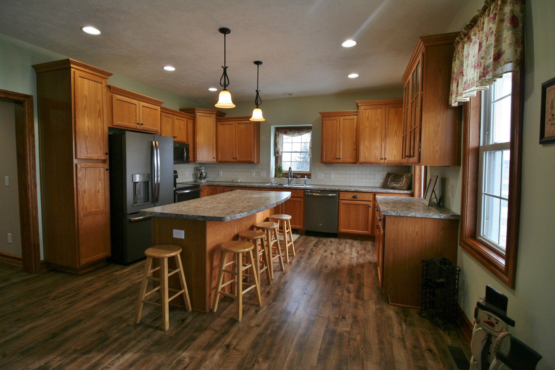 Spacious kitchen with wood cabinets, island with stools, stainless steel appliances, and wood flooring.