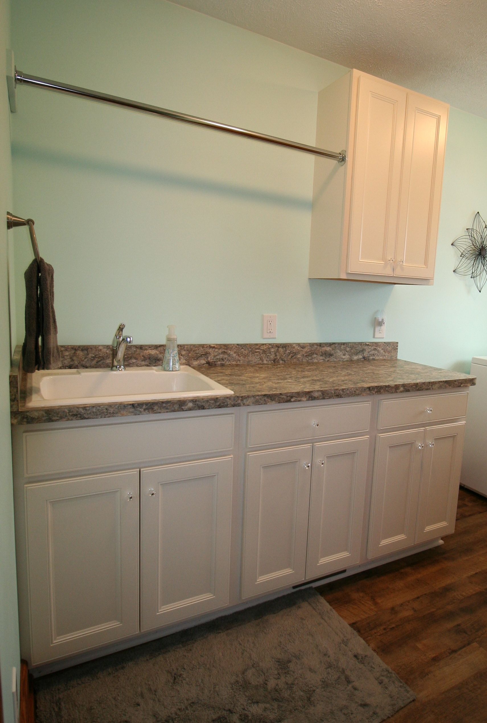 Laundry room with sink, countertop, cabinets, drying rack, and blue wall.