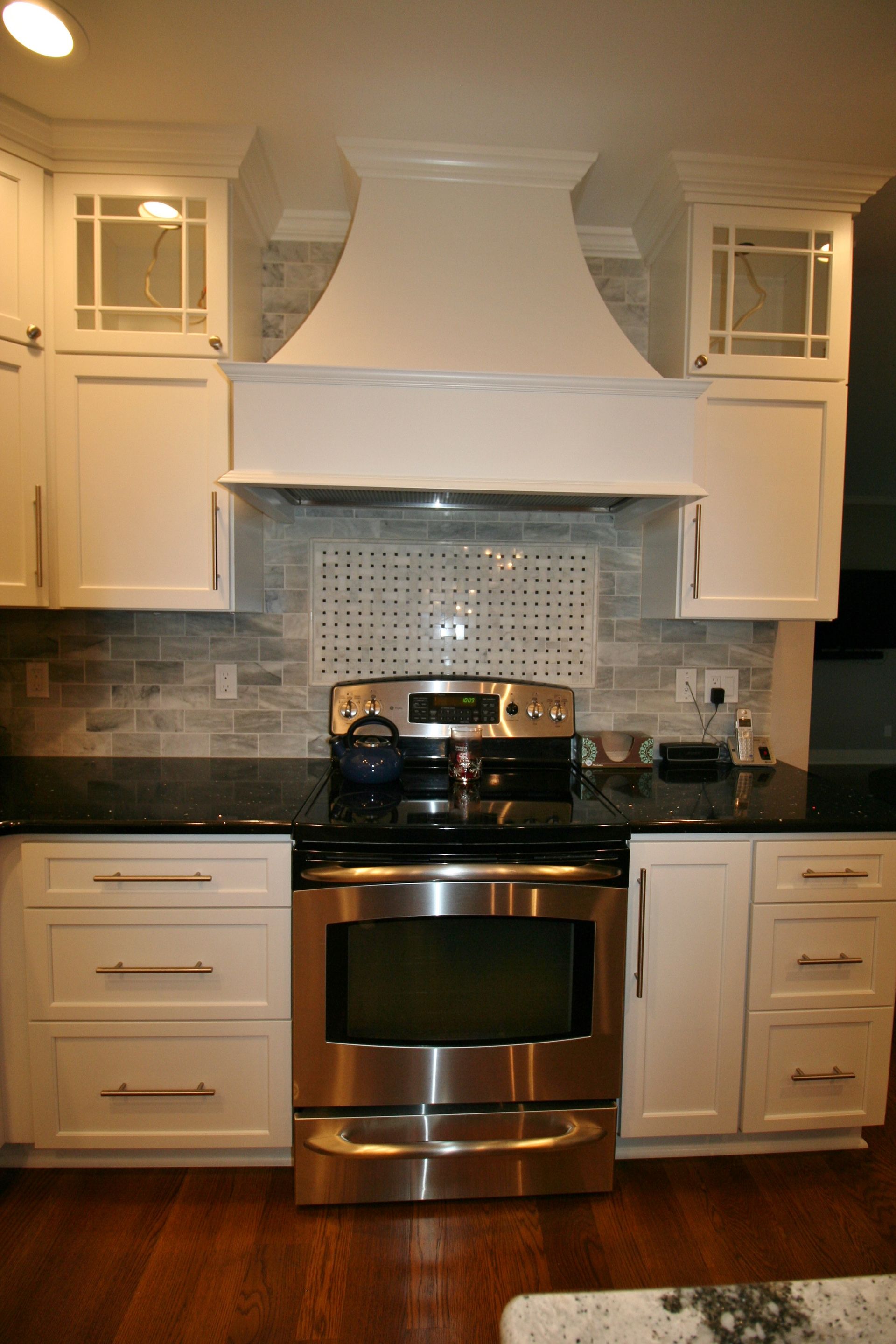 Stainless steel oven in a white kitchen with a decorative range hood and dark countertops.
