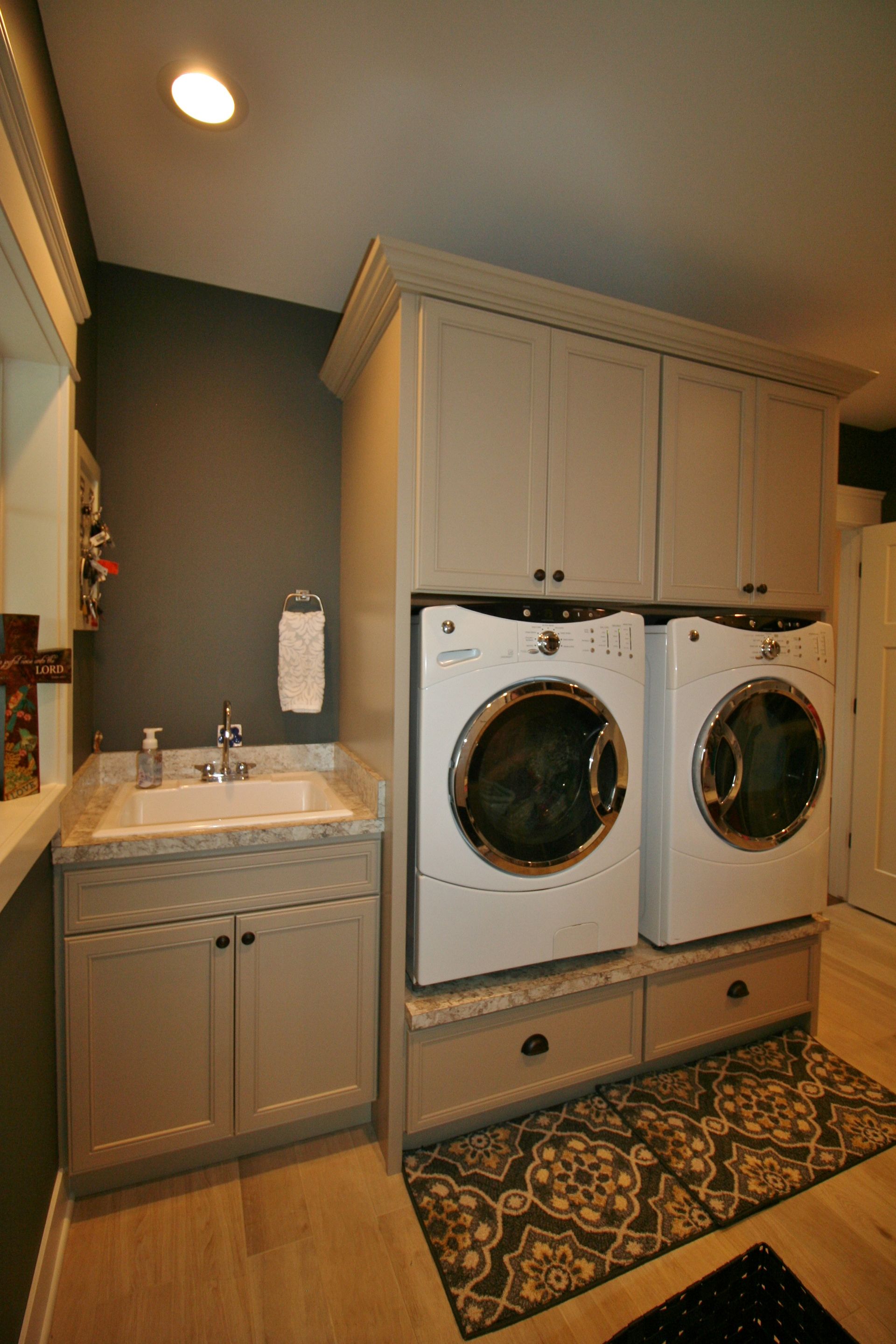 Laundry room with stacked washer/dryer, sink, and cabinets; neutral colors.