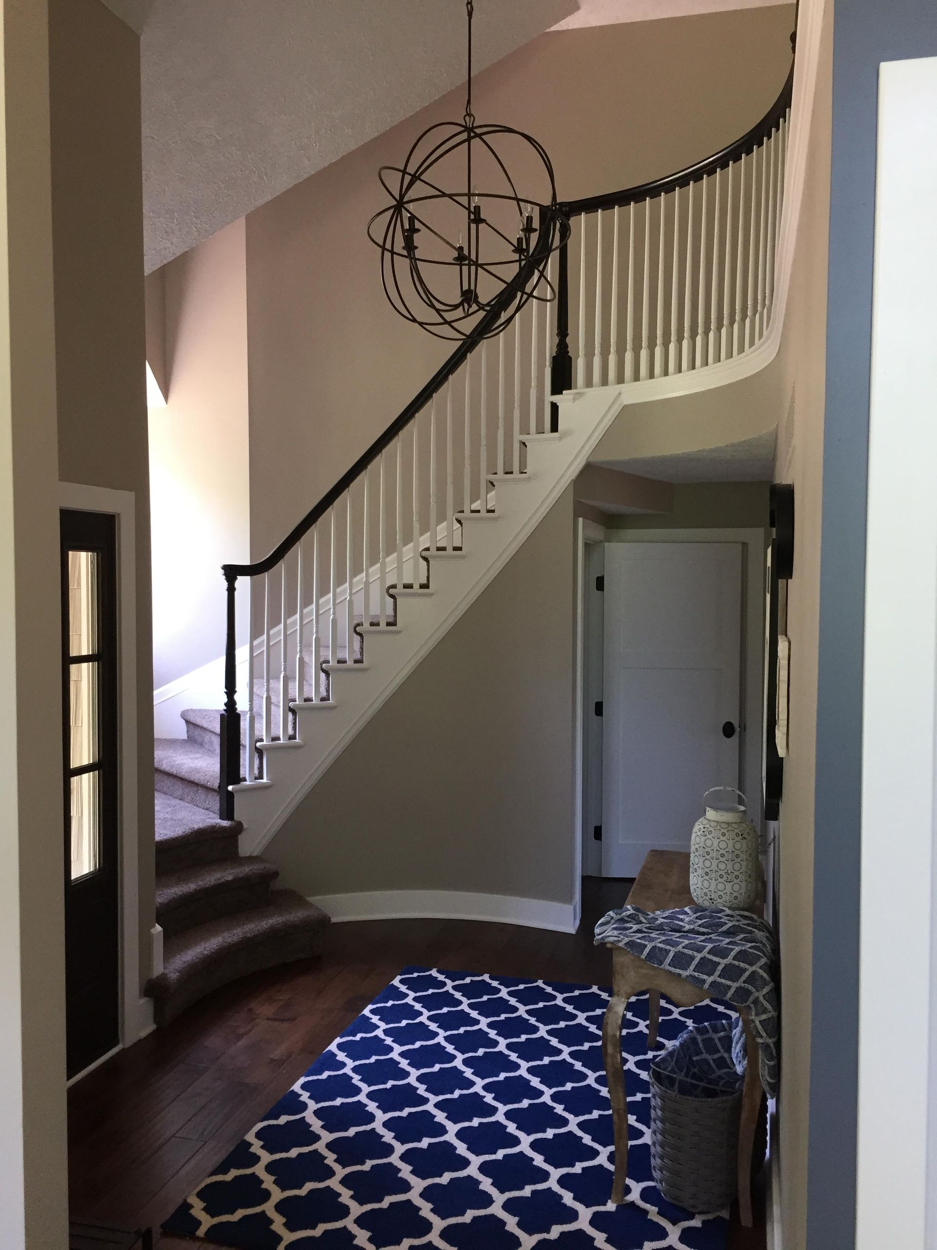 A curved staircase with white spindles, dark wood railing, and a blue patterned rug in a home's entryway.