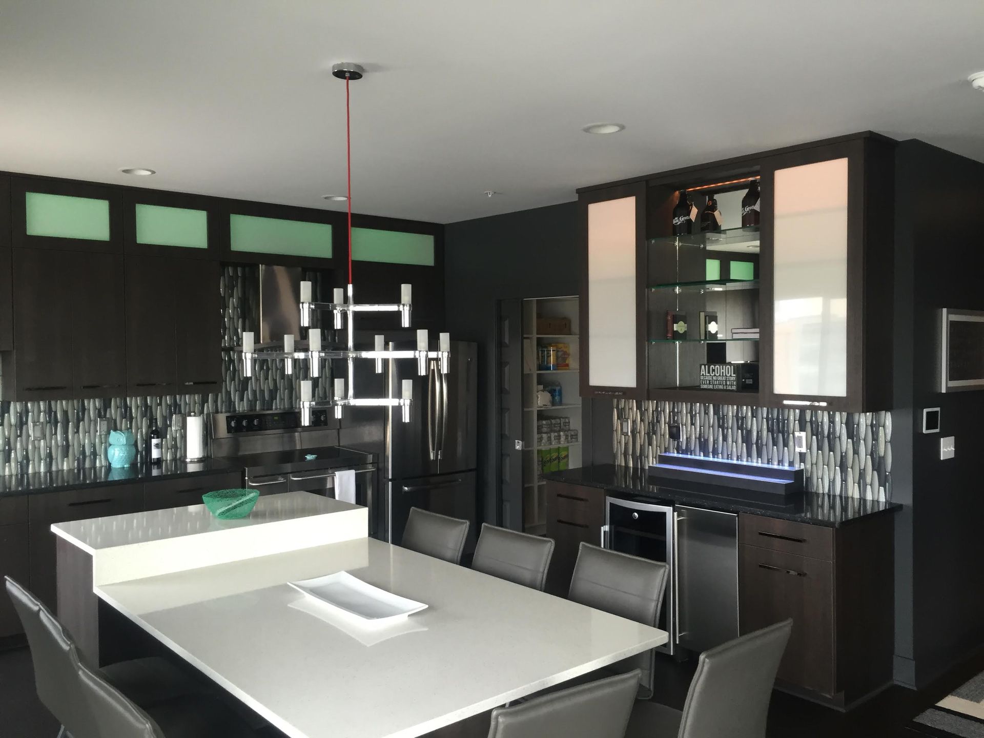 Modern kitchen with dark cabinetry, white countertops, and a dining island with seating.