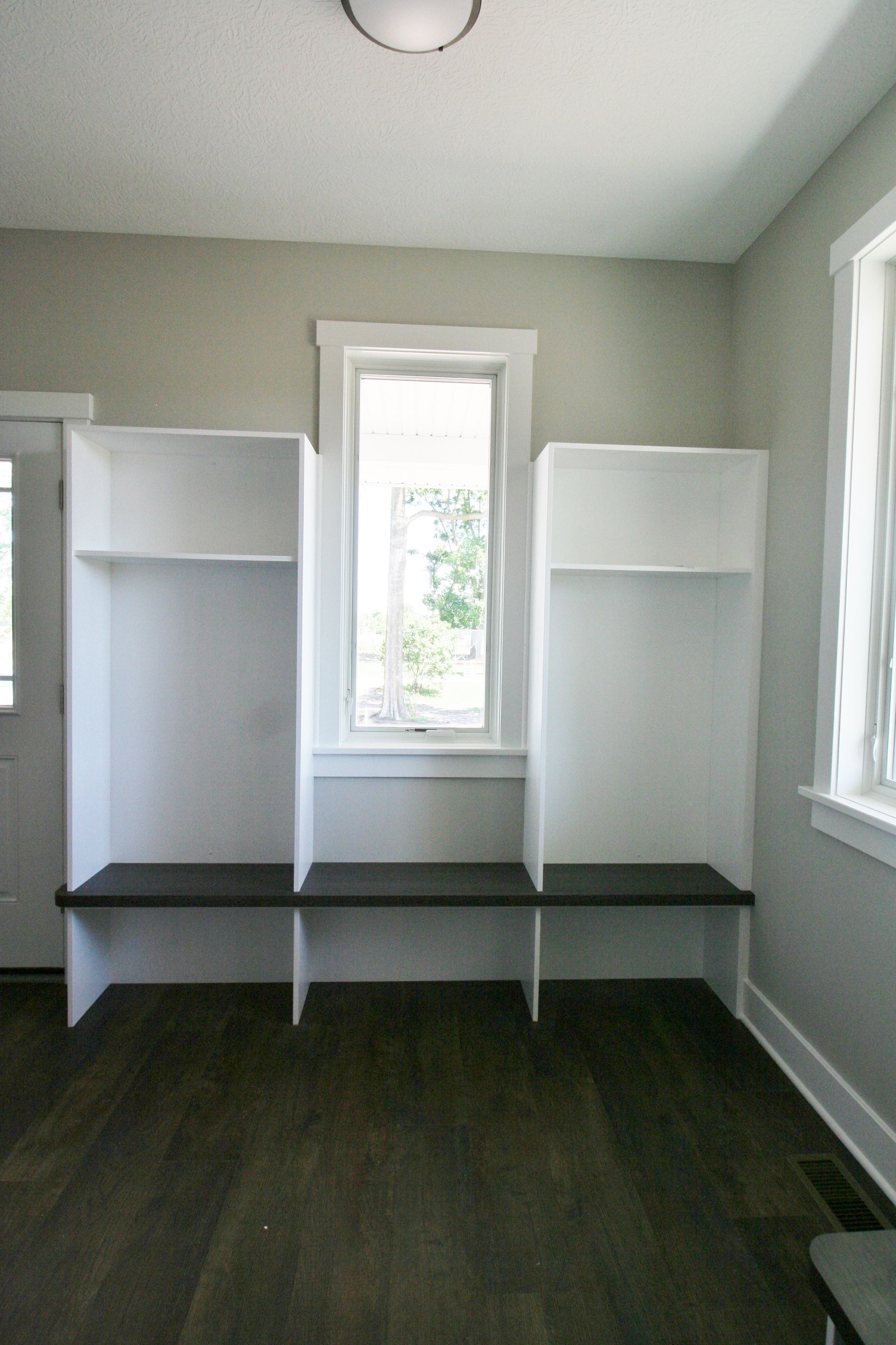 Built-in white storage unit with bench and window. Dark wood floor and gray walls.