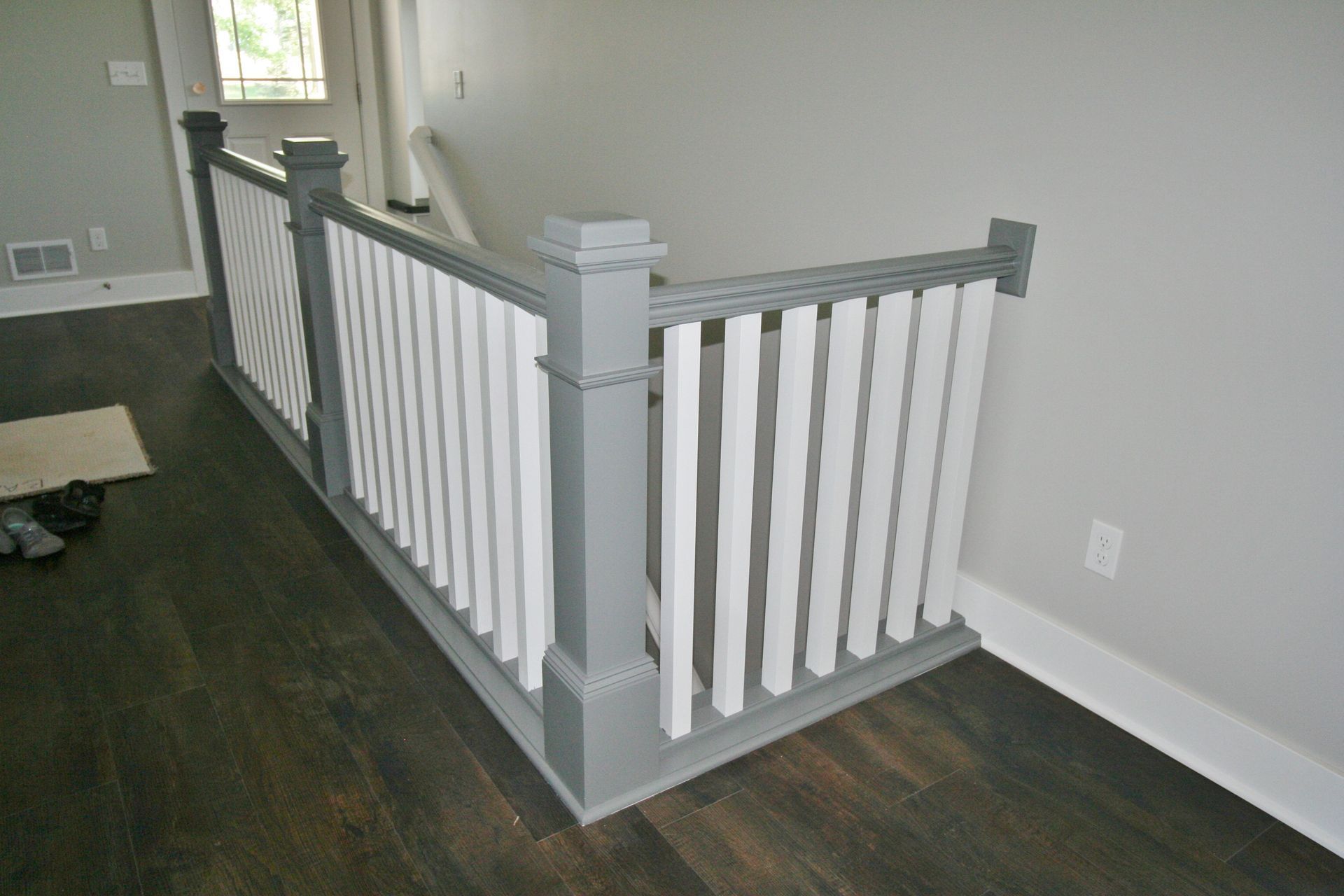 Grey and white painted staircase railing. Wooden planks stand vertically between gray posts.