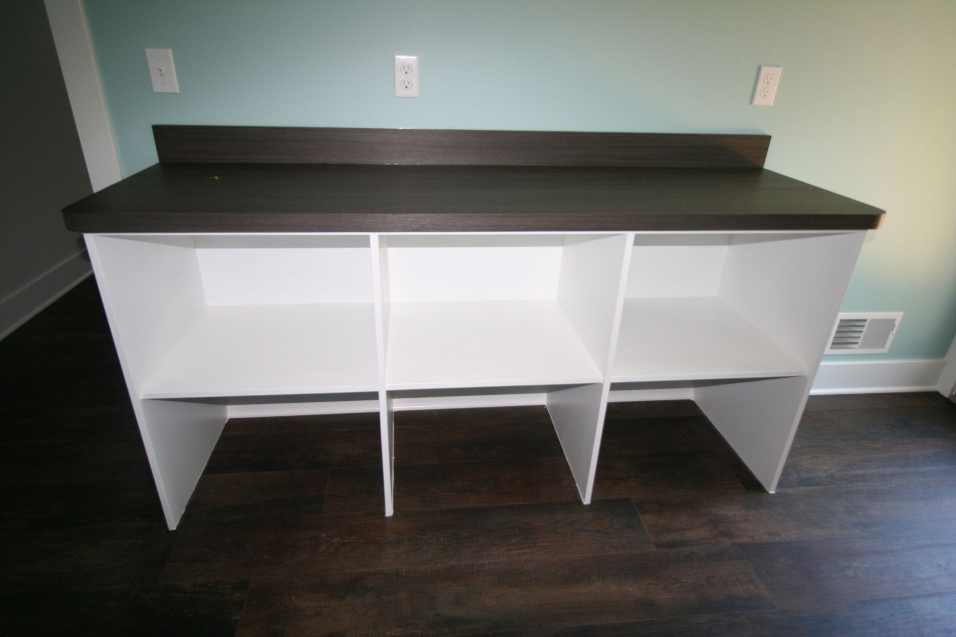 White shelving unit with dark countertop against a teal wall.