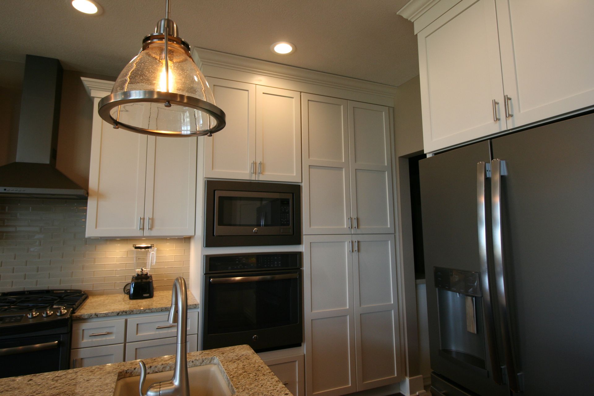 Kitchen with white cabinets, stainless steel appliances, and pendant light over granite countertop.