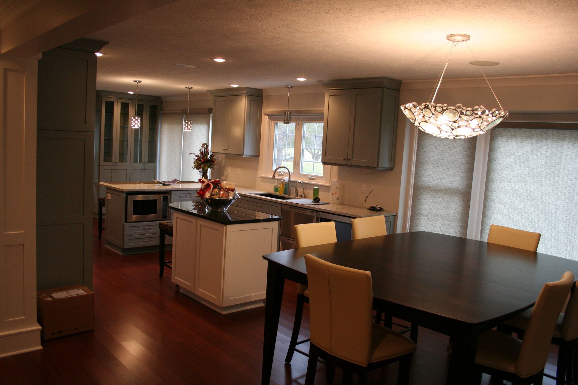 Modern kitchen with dark wood floors, gray cabinets, a black island, and a dining table with tan chairs.