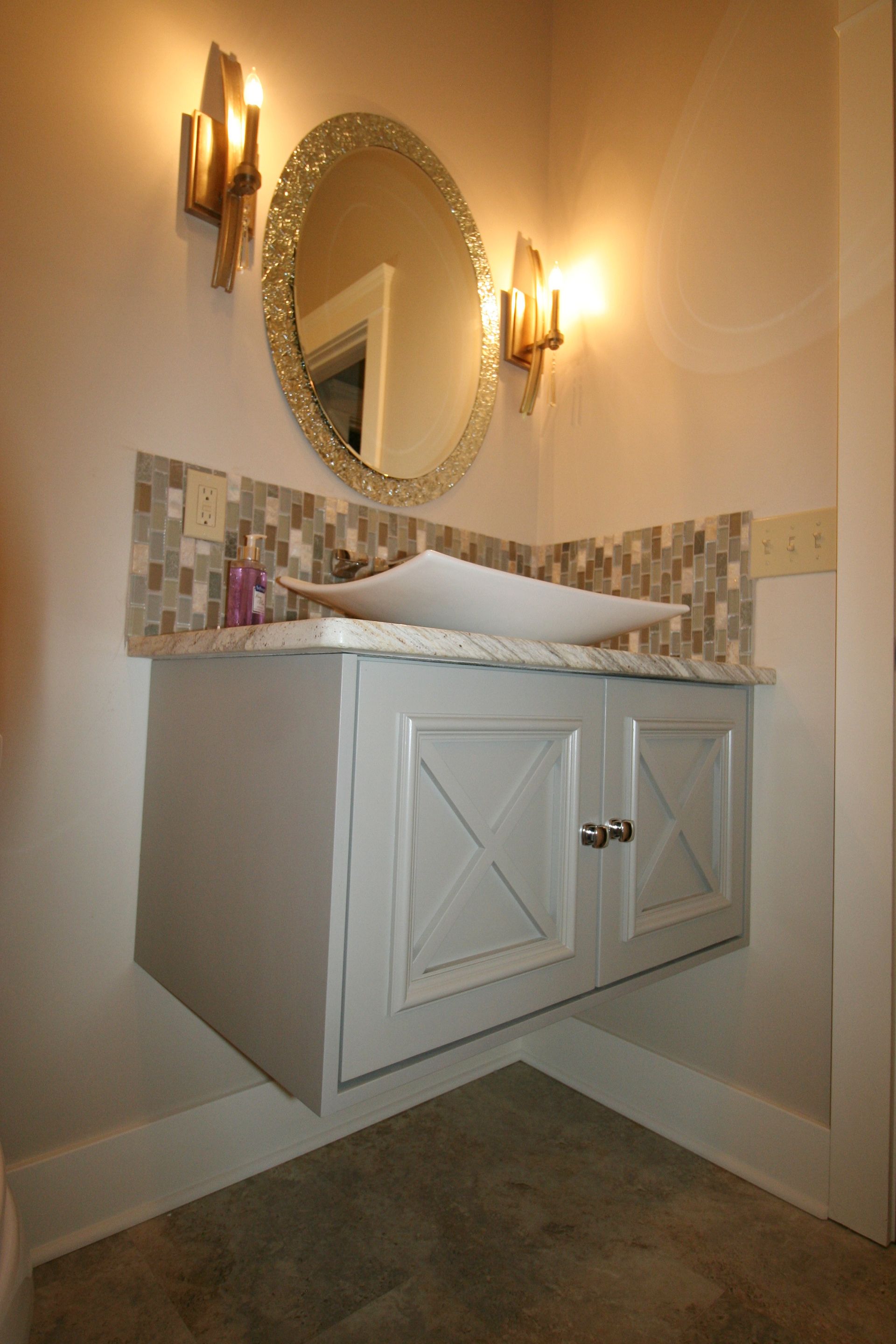 Floating vanity with white countertop and vessel sink, mosaic backsplash, and ornate mirror.