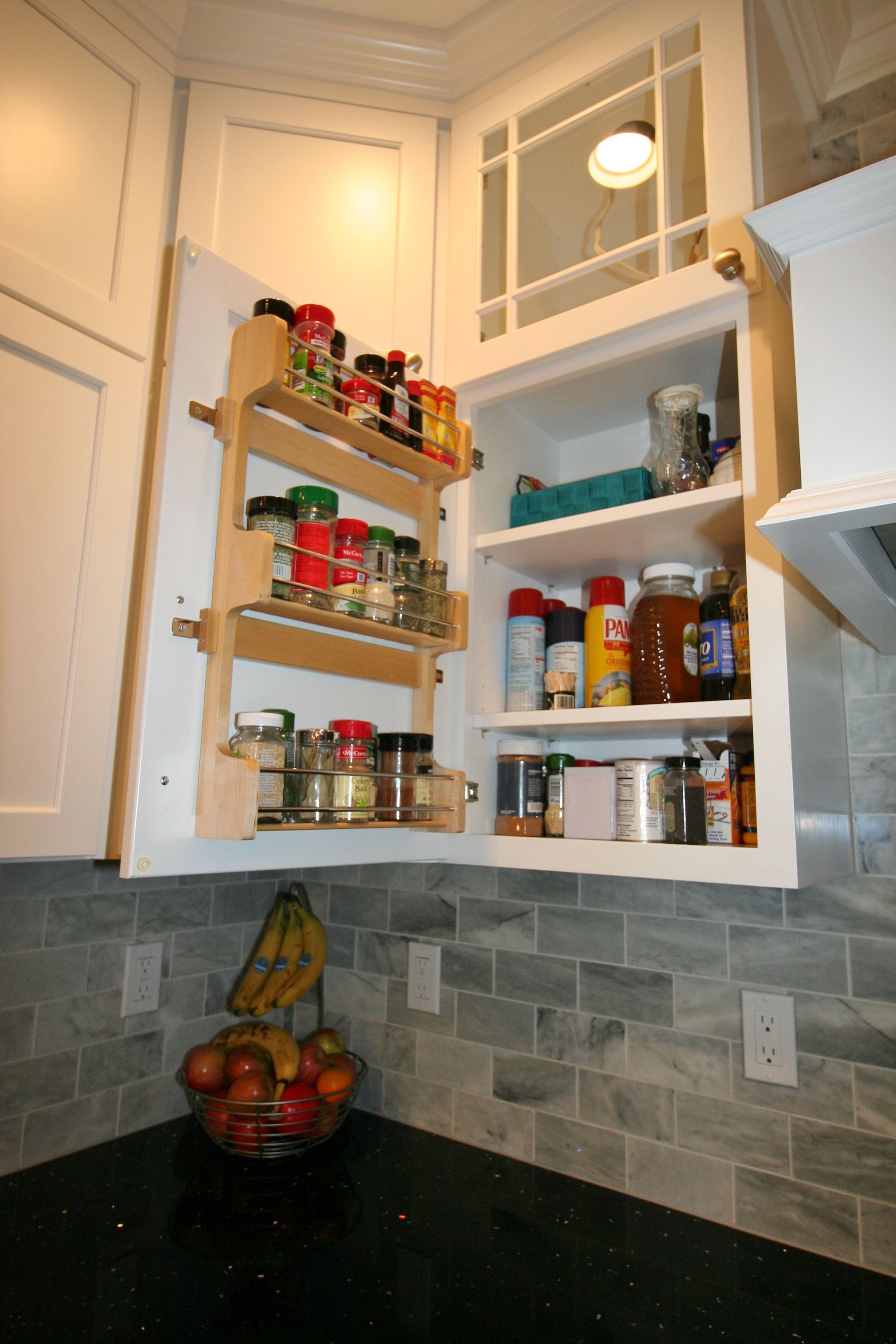 Kitchen cabinet open, with pull-out spice rack and shelves containing various food items and cleaning supplies.