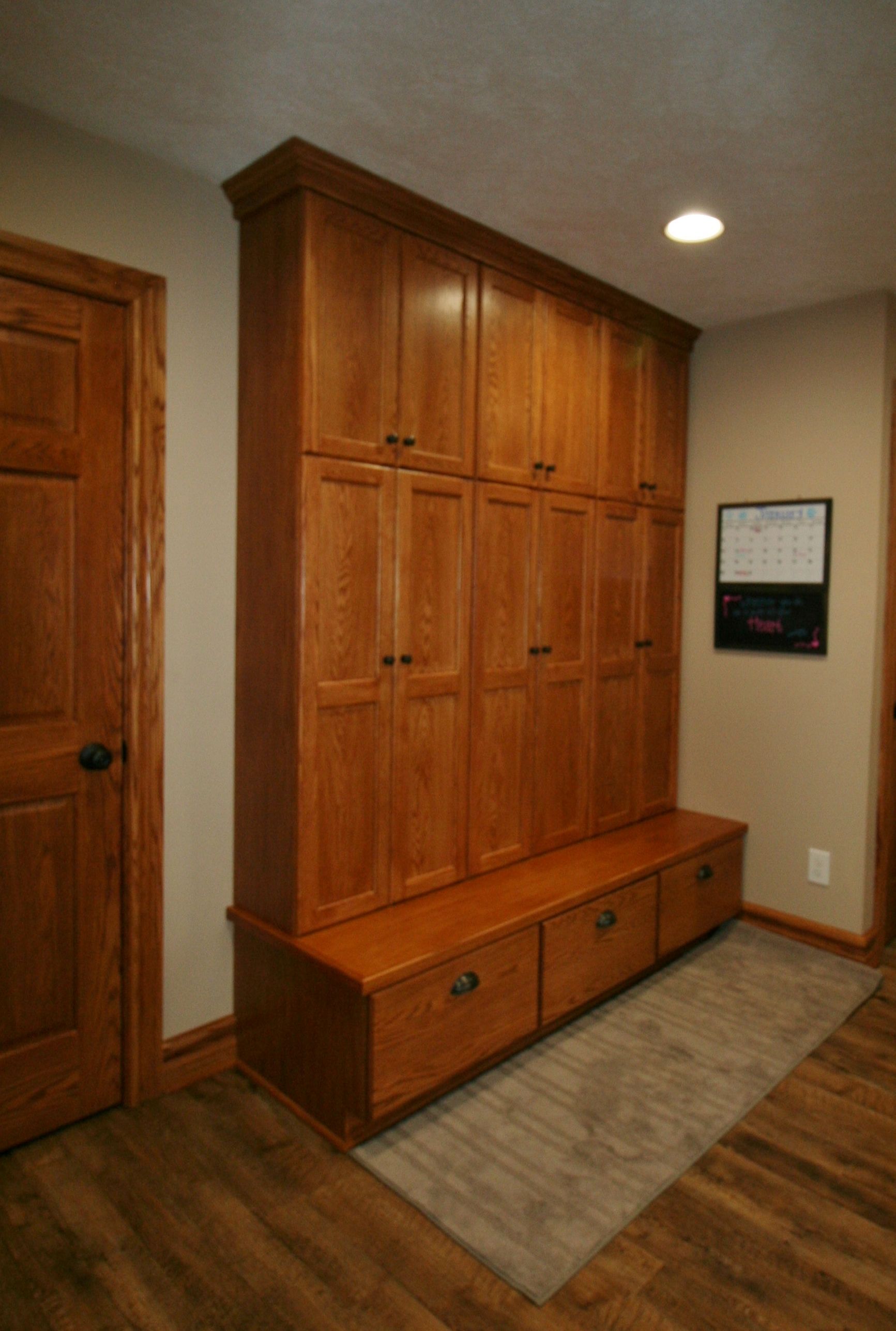 Wooden mudroom storage with cabinets, bench, and drawers; brown tones.