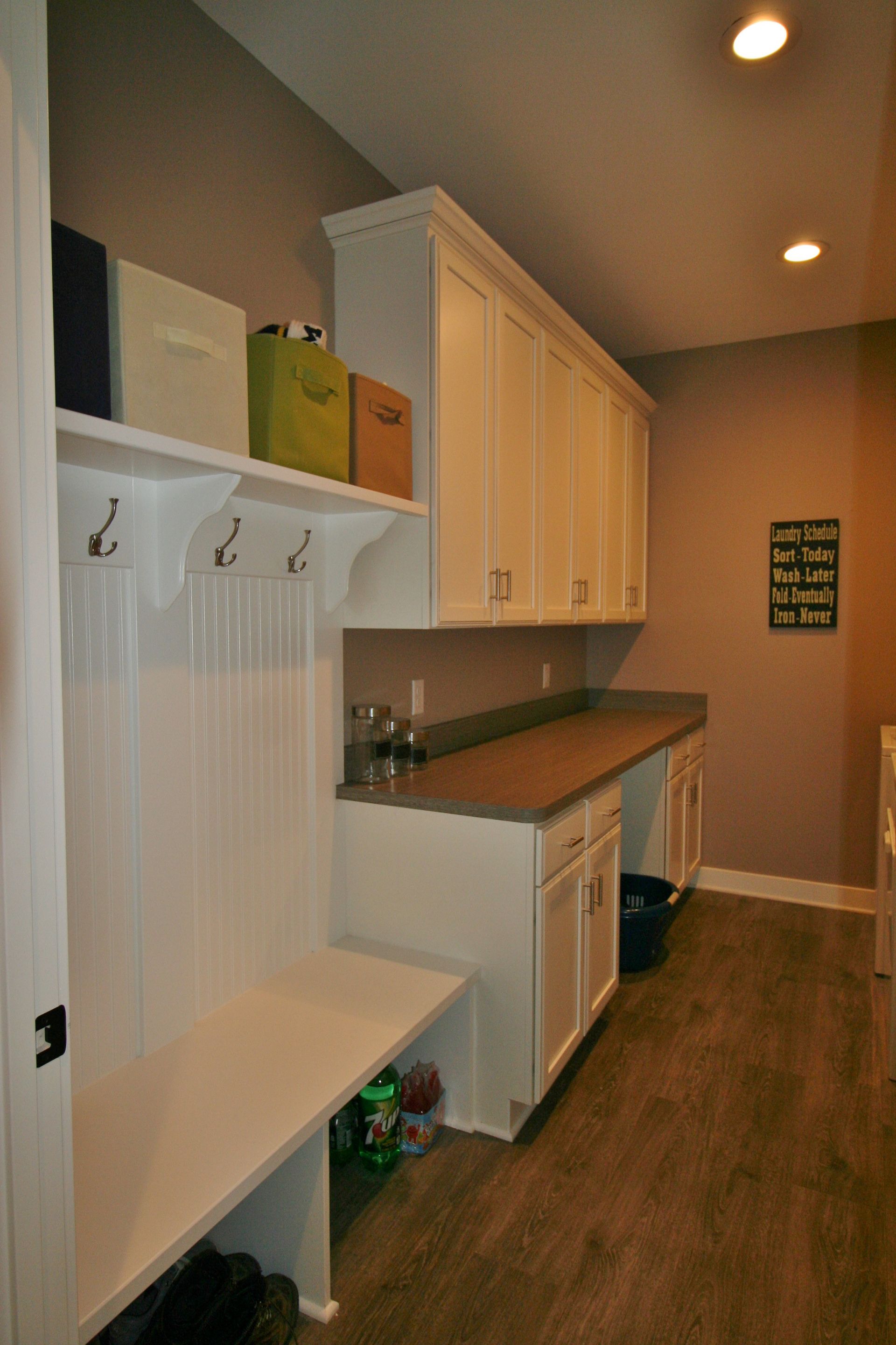 Mudroom with white cabinets, bench, and hooks. Brown countertop. Wooden floor.