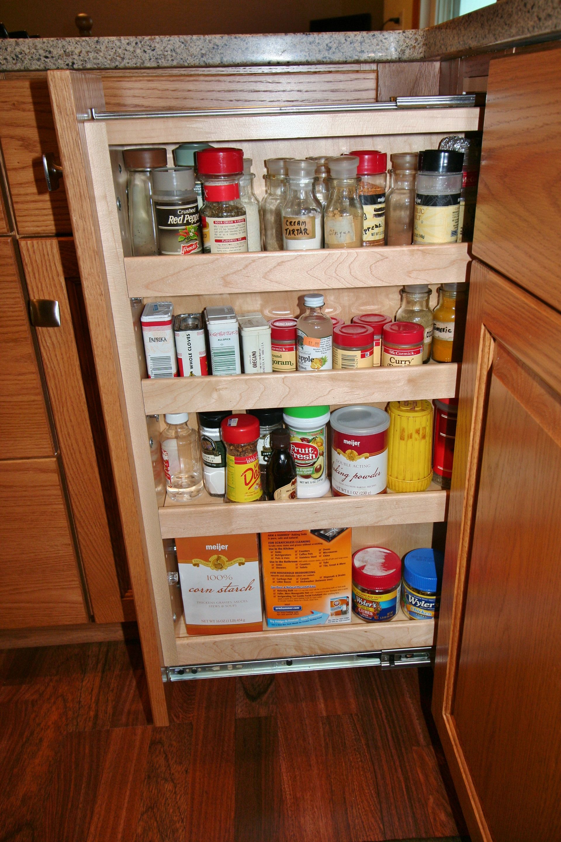 Wooden pull-out spice rack filled with various spice containers inside a kitchen cabinet.