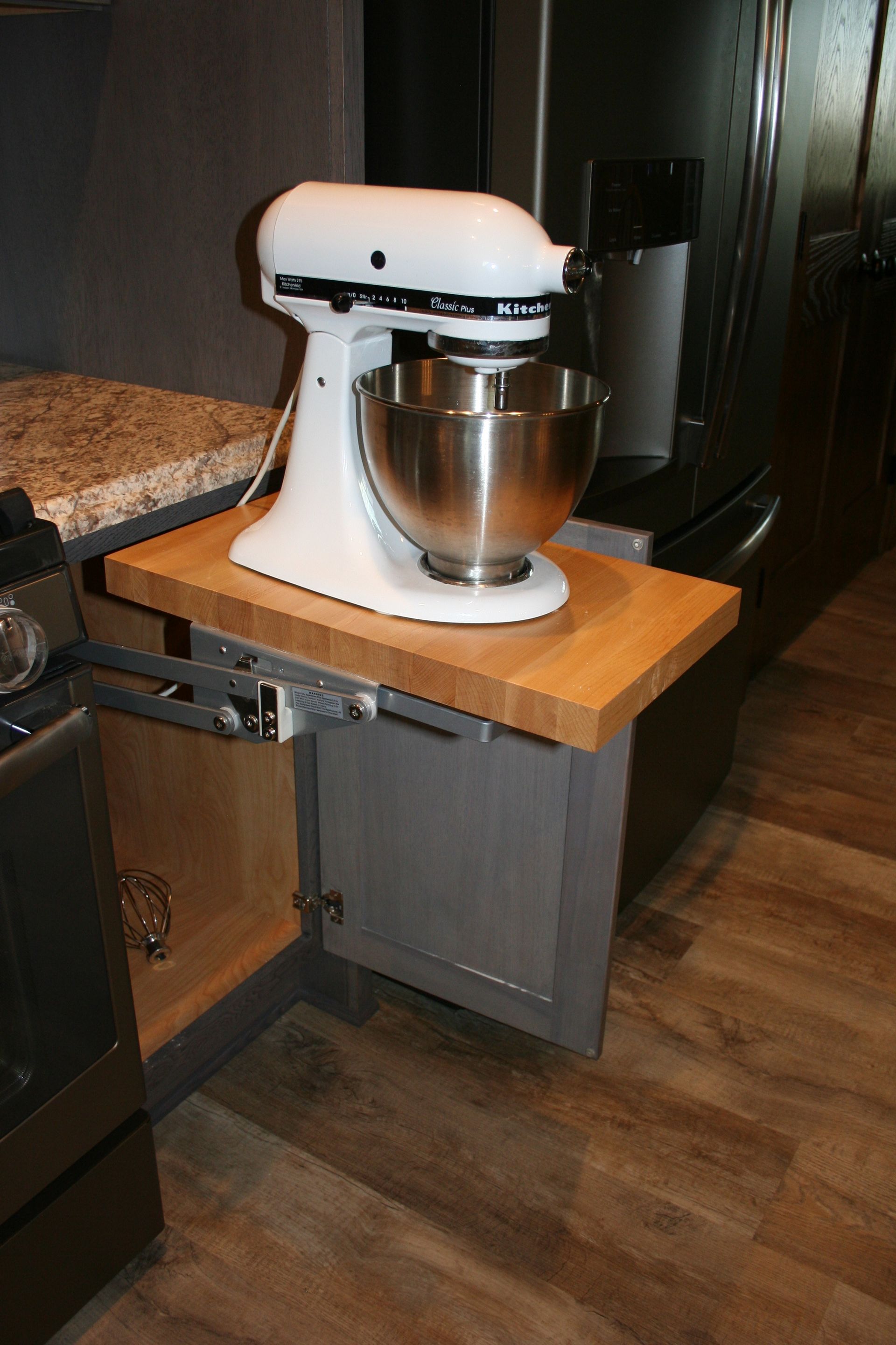 Kitchen cabinet with a pull-out shelf holding a white stand mixer. Gray cabinet, butcher block shelf.