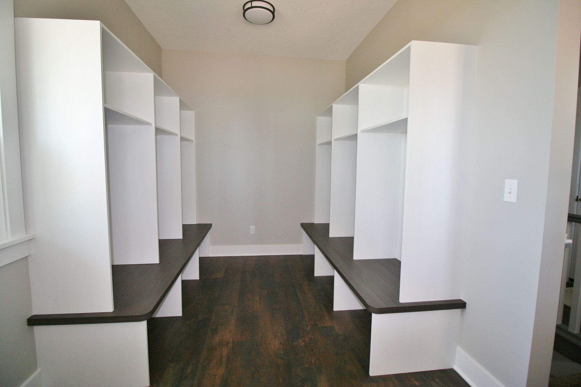 Hallway with white storage lockers and dark wood benches. Gray walls, dark hardwood floor.