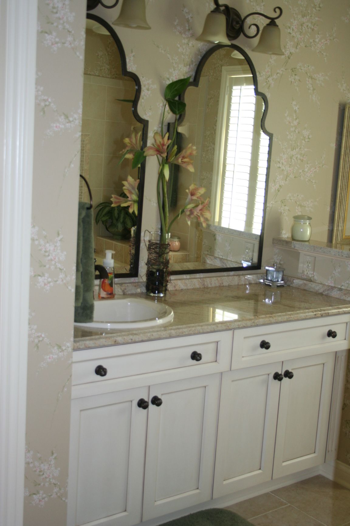 Bathroom vanity with white cabinets, ornate mirrors, and a floral arrangement.