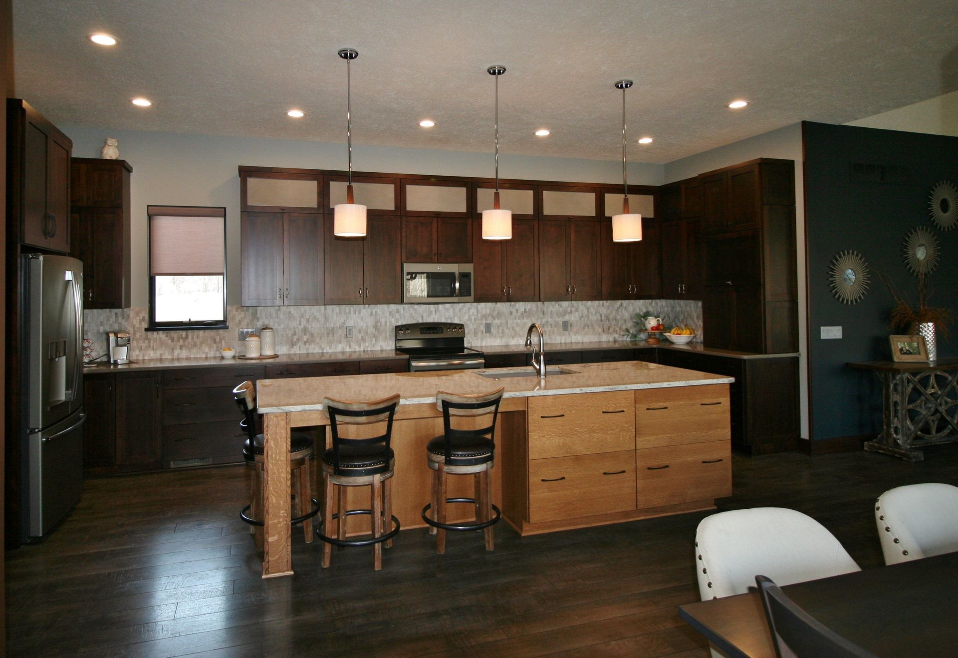 Modern kitchen with dark brown cabinets, light countertops, and wooden island with three pendant lights.