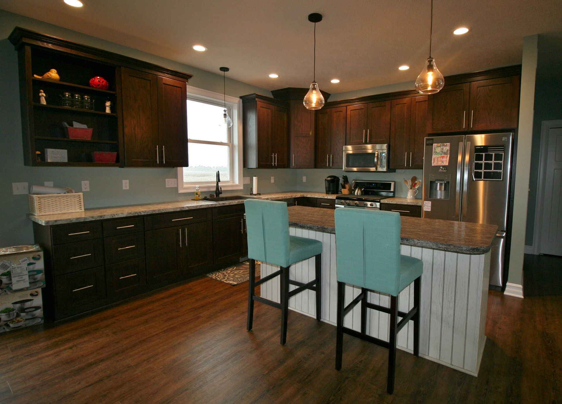 Modern kitchen with dark cabinetry, light countertops, island with teal stools, and stainless steel appliances.