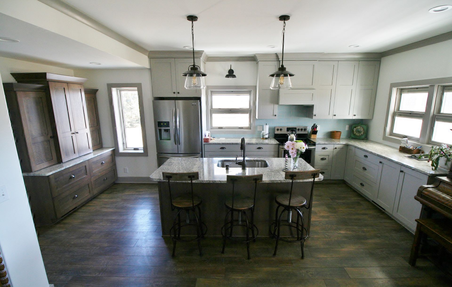 Spacious kitchen with gray cabinets, island with stools, stainless steel appliances, and wooden floors.