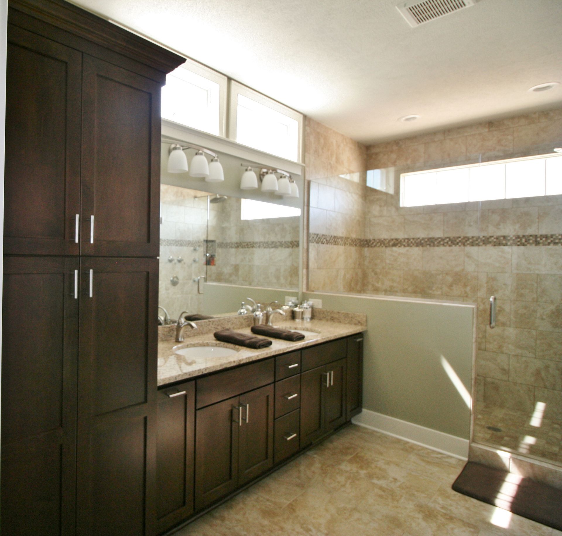 Dark wood bathroom with vanity, shower, and tall storage cabinet; beige walls and floor.