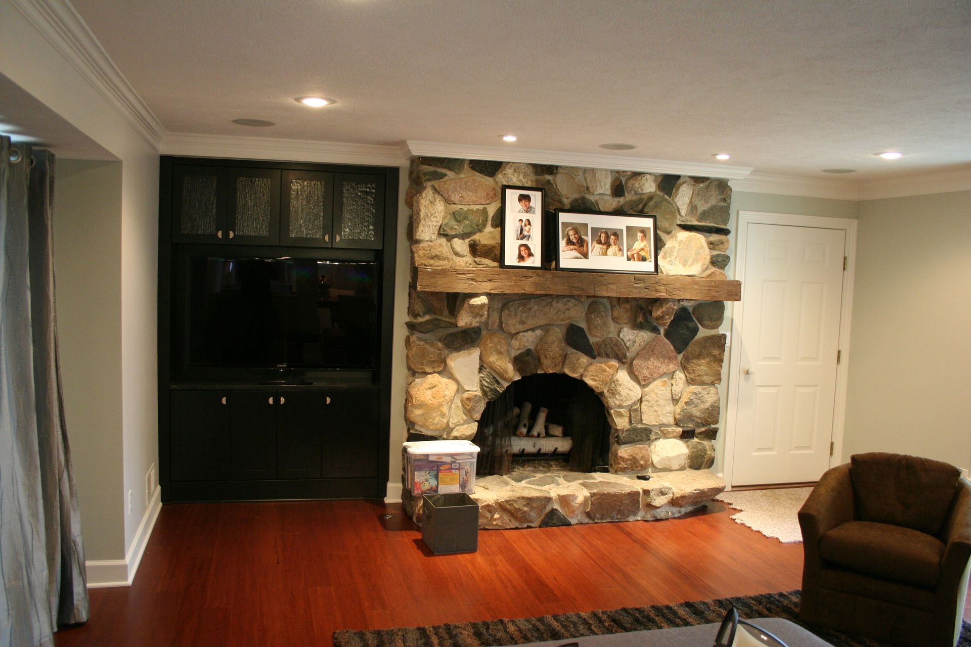 A living room with a stone fireplace, TV cabinet, hardwood floor, and a door.