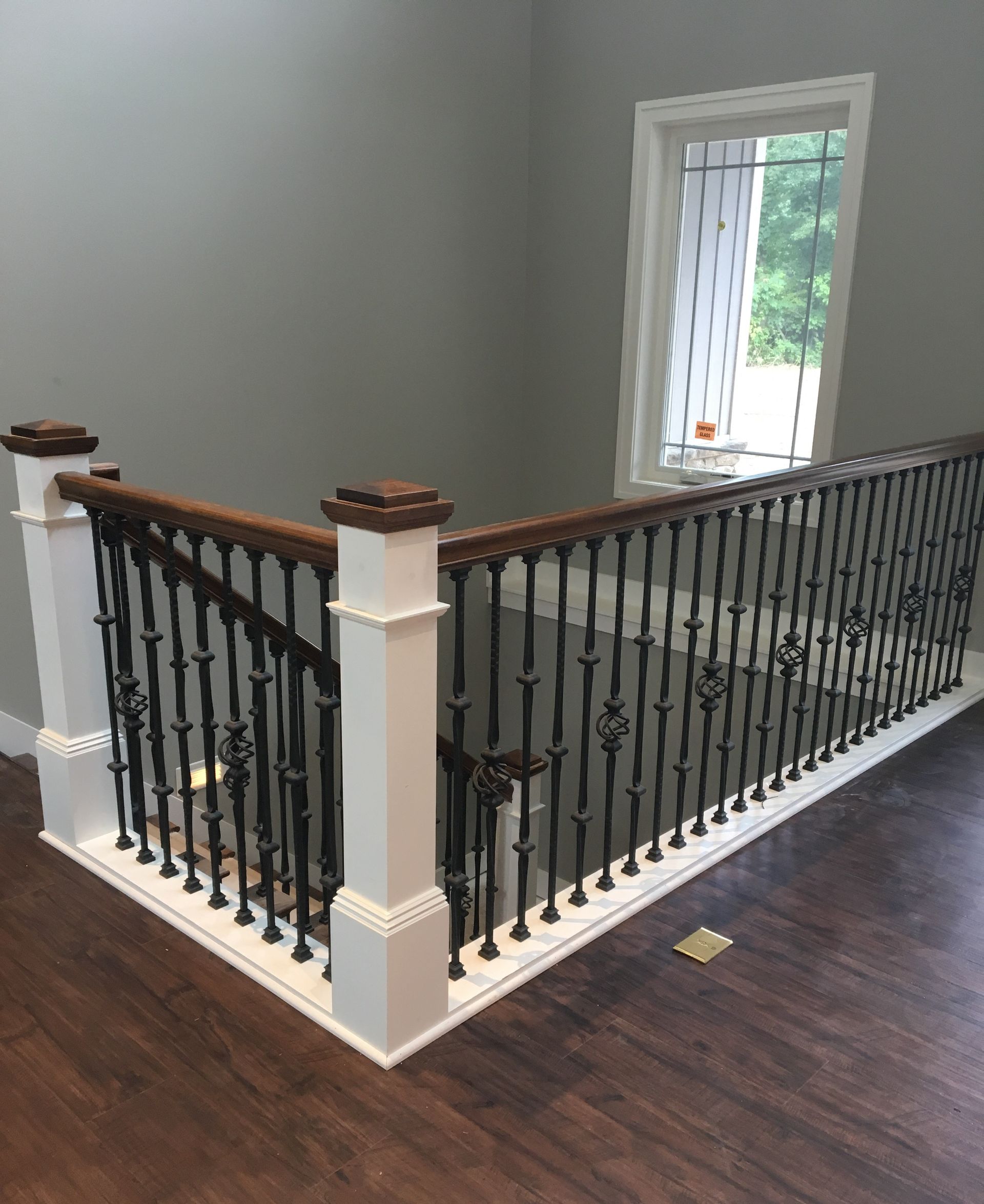 Dark wooden staircase with black iron railing, white posts, and gray wall.