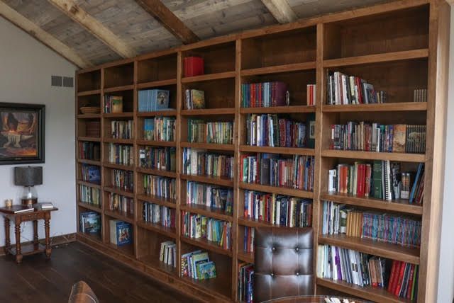 Large wooden bookcase filled with books against a wall. A desk and small table are in front.