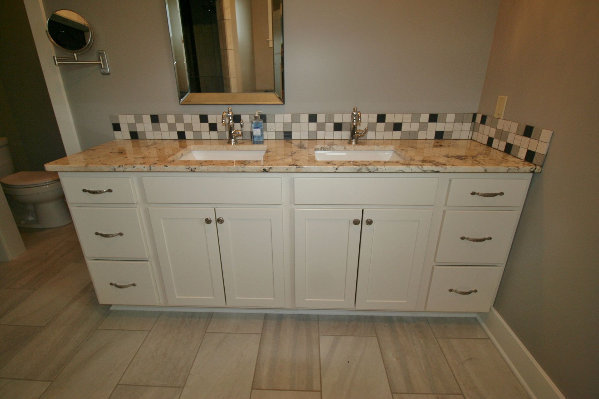 Double bathroom vanity with white cabinets, granite countertop, and tiled backsplash.