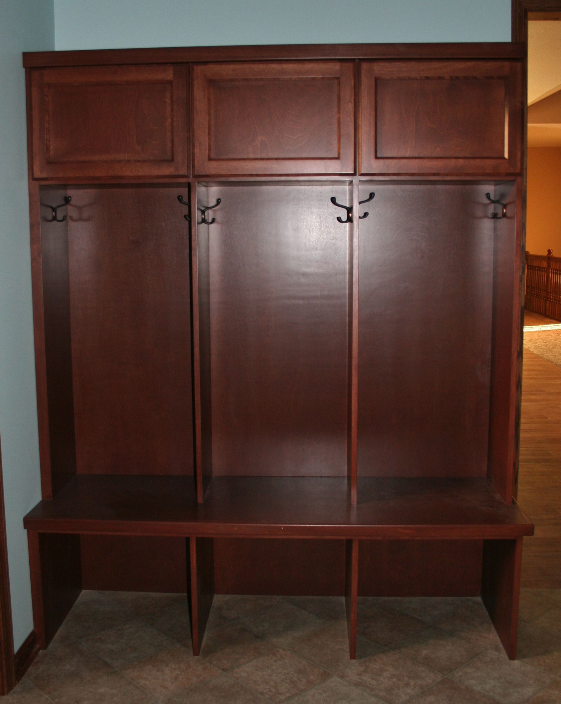 Brown wooden entryway storage unit with hooks, cabinets, and a bench.