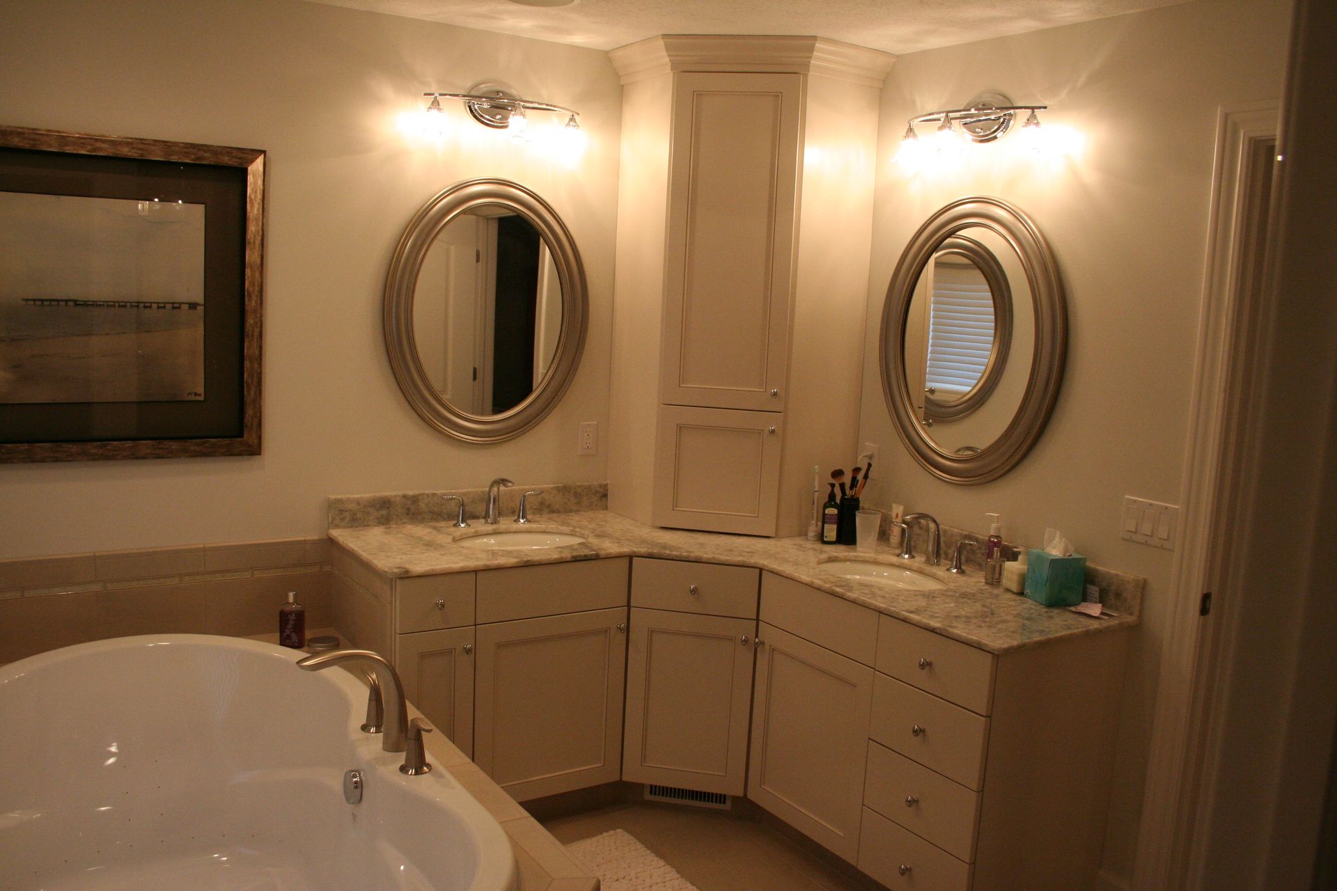 Bathroom with corner vanity, oval mirrors, and built-in cabinet. Bathtub in foreground.