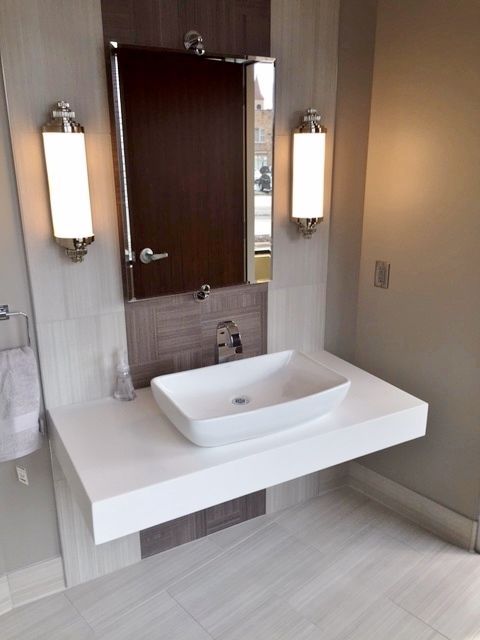White floating sink and countertop with rectangular mirror and two sconces in a bathroom.