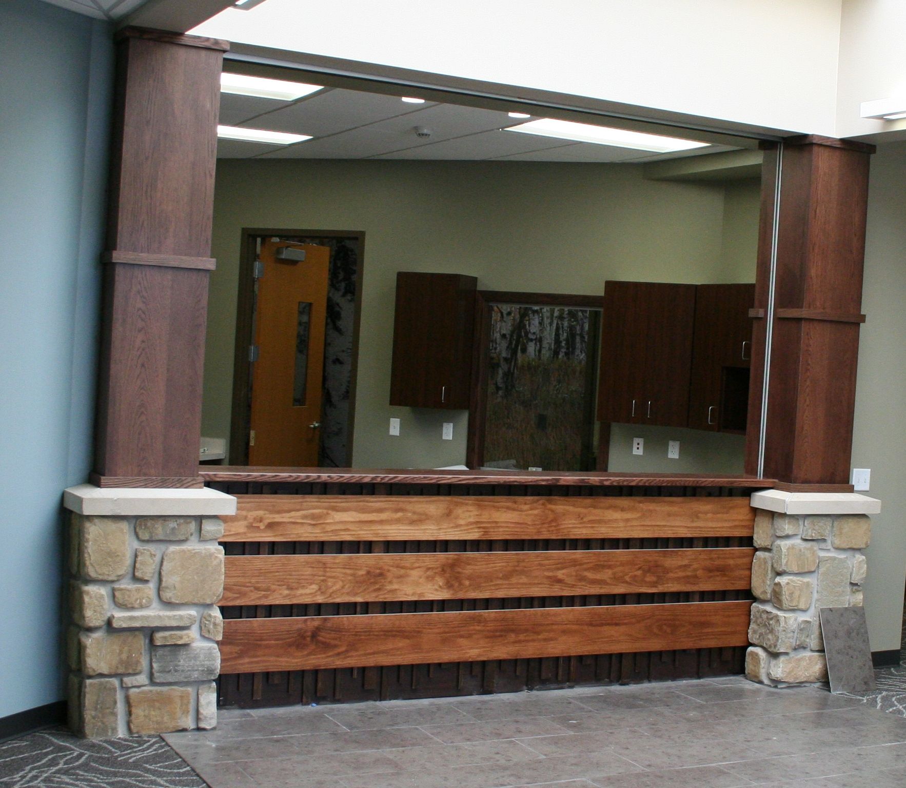 Wooden reception desk with stone columns, interior view, open to a back office.
