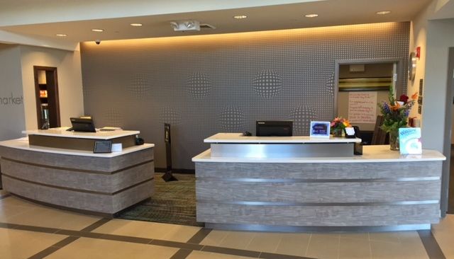 Hotel reception desk with two counters, gray paneling, and a neutral color scheme.