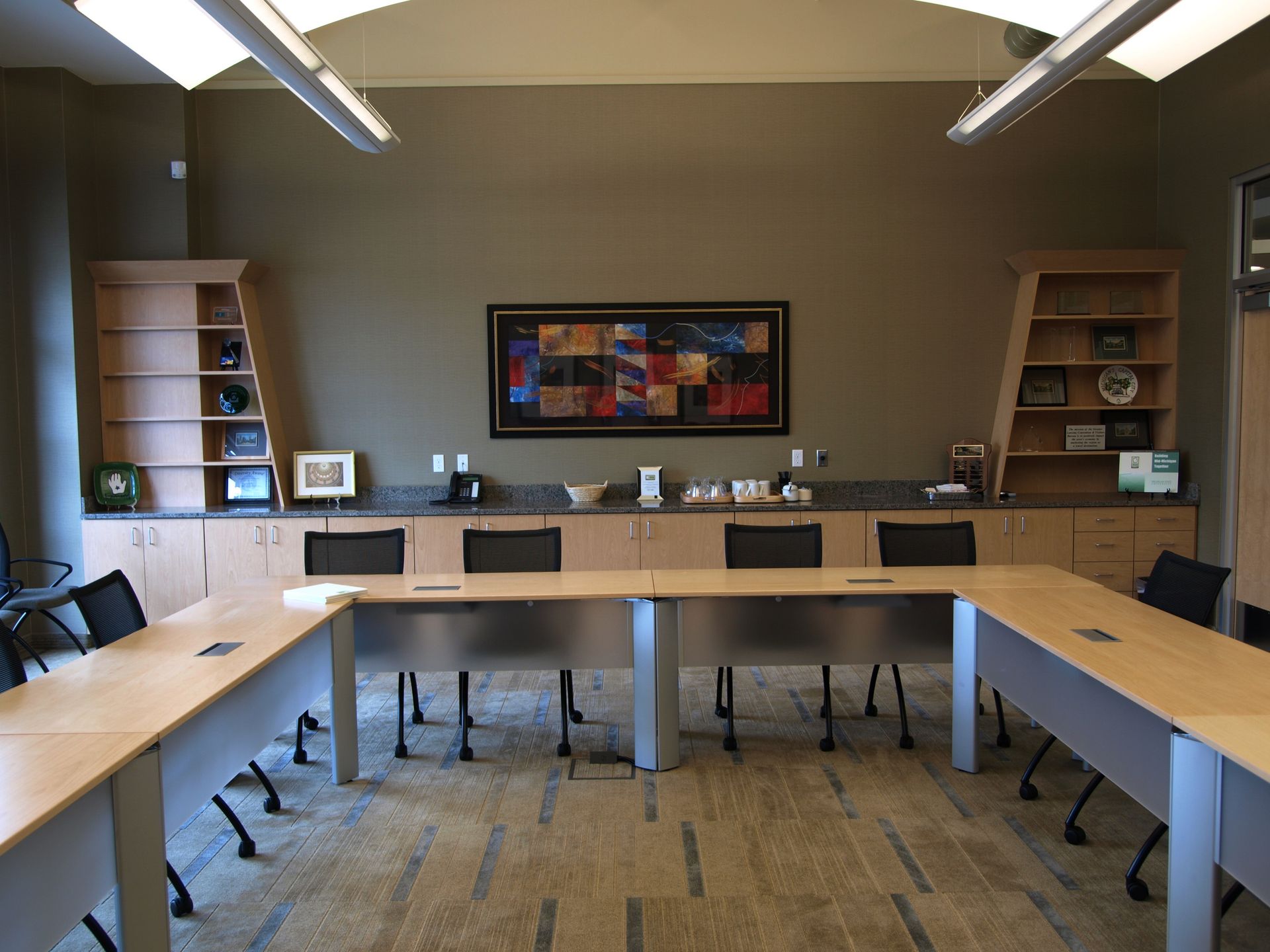 Conference room with a U-shaped table, cabinets, and a colorful abstract painting on the wall.