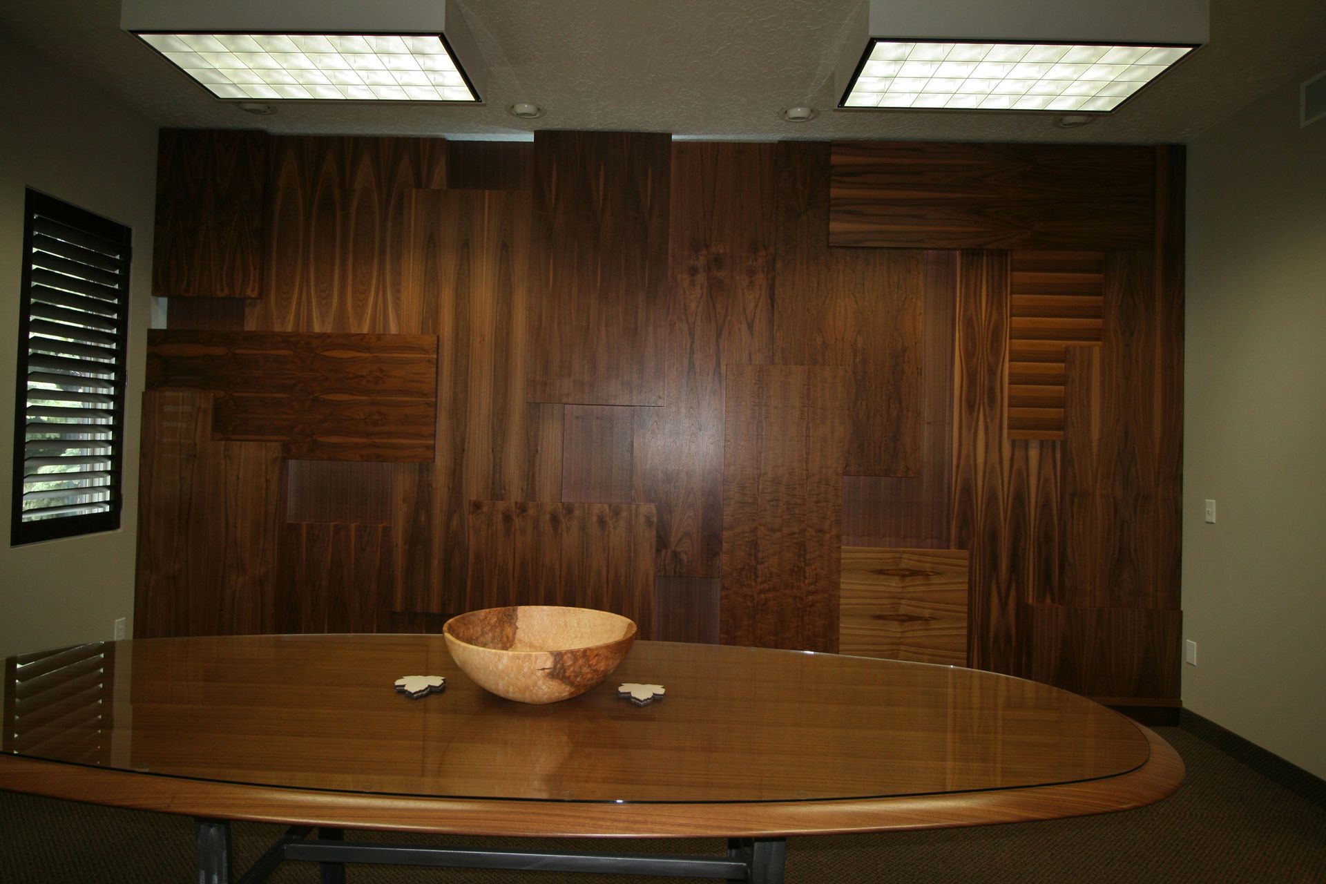Oval wooden table with a bowl on it, in front of a textured wood panel wall.