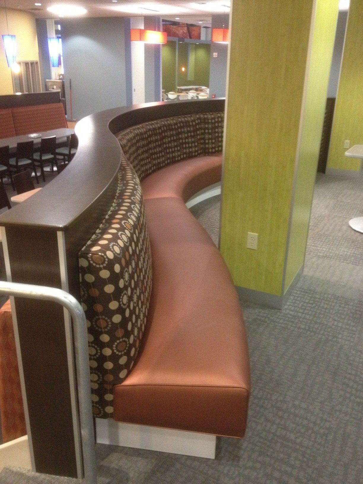 Curved booth seating in a dining area. Brown leather seat, patterned back, dark wood trim, and a yellow column.