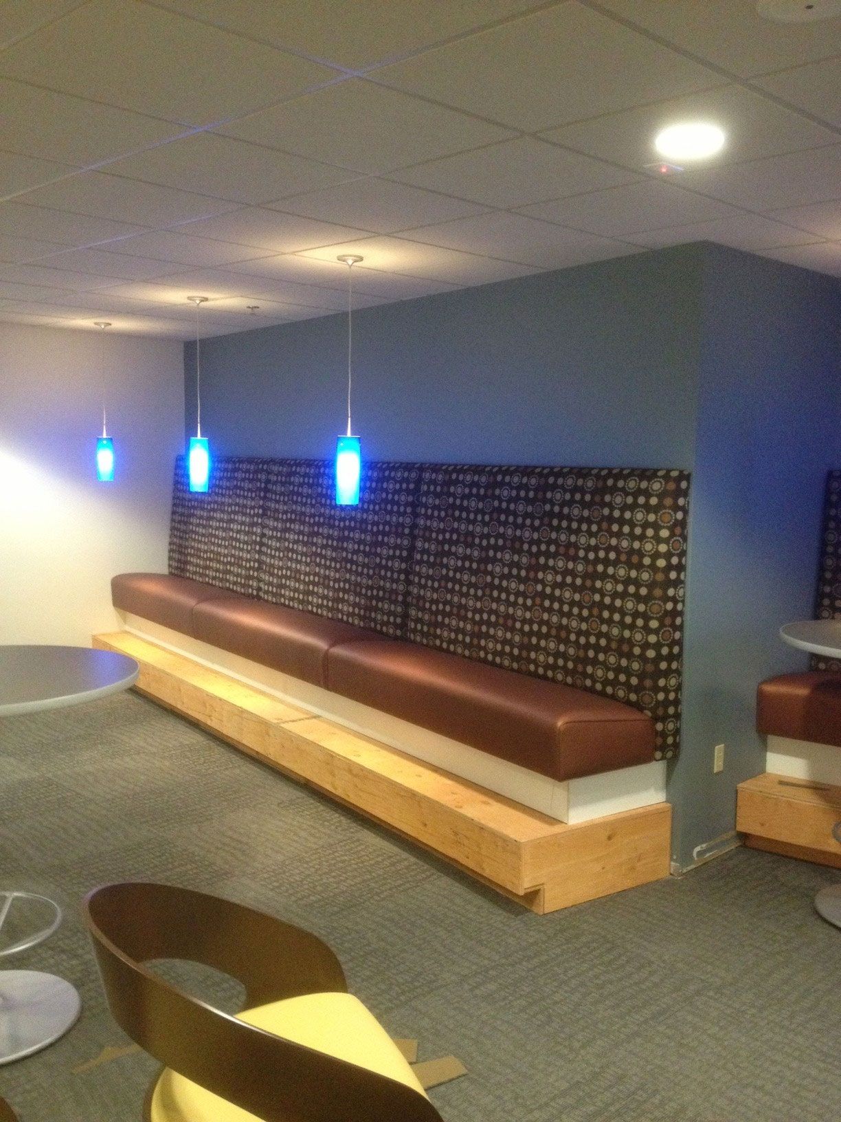 Built-in booth seating in a room. Brown leather bench, patterned back, blue pendant lights.