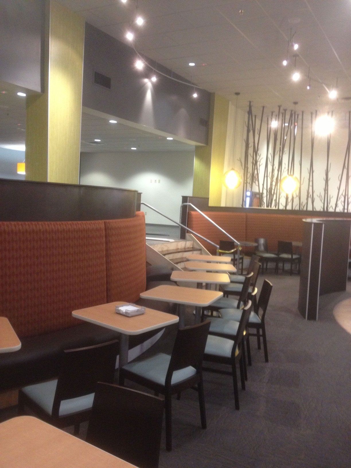 Restaurant interior with booth seating and tables. Orange and black seating, tan tables, and dark chairs.