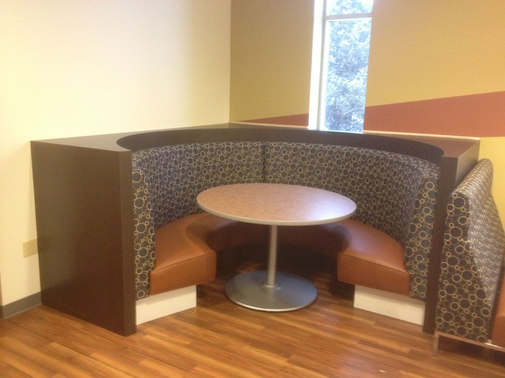 Booth seating with a circular table and two brown and patterned benches. Window in the background.