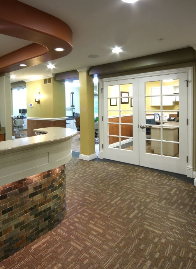 Reception area with curved desk, patterned carpet, and double doors to an office.
