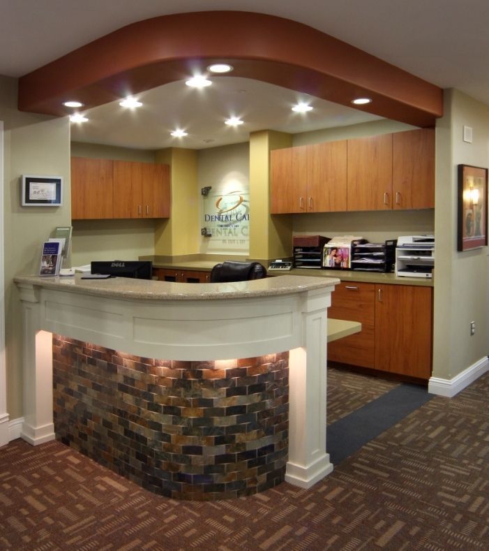 Reception area of a dental office with a stone-accented front desk, wood cabinets, and recessed lighting.