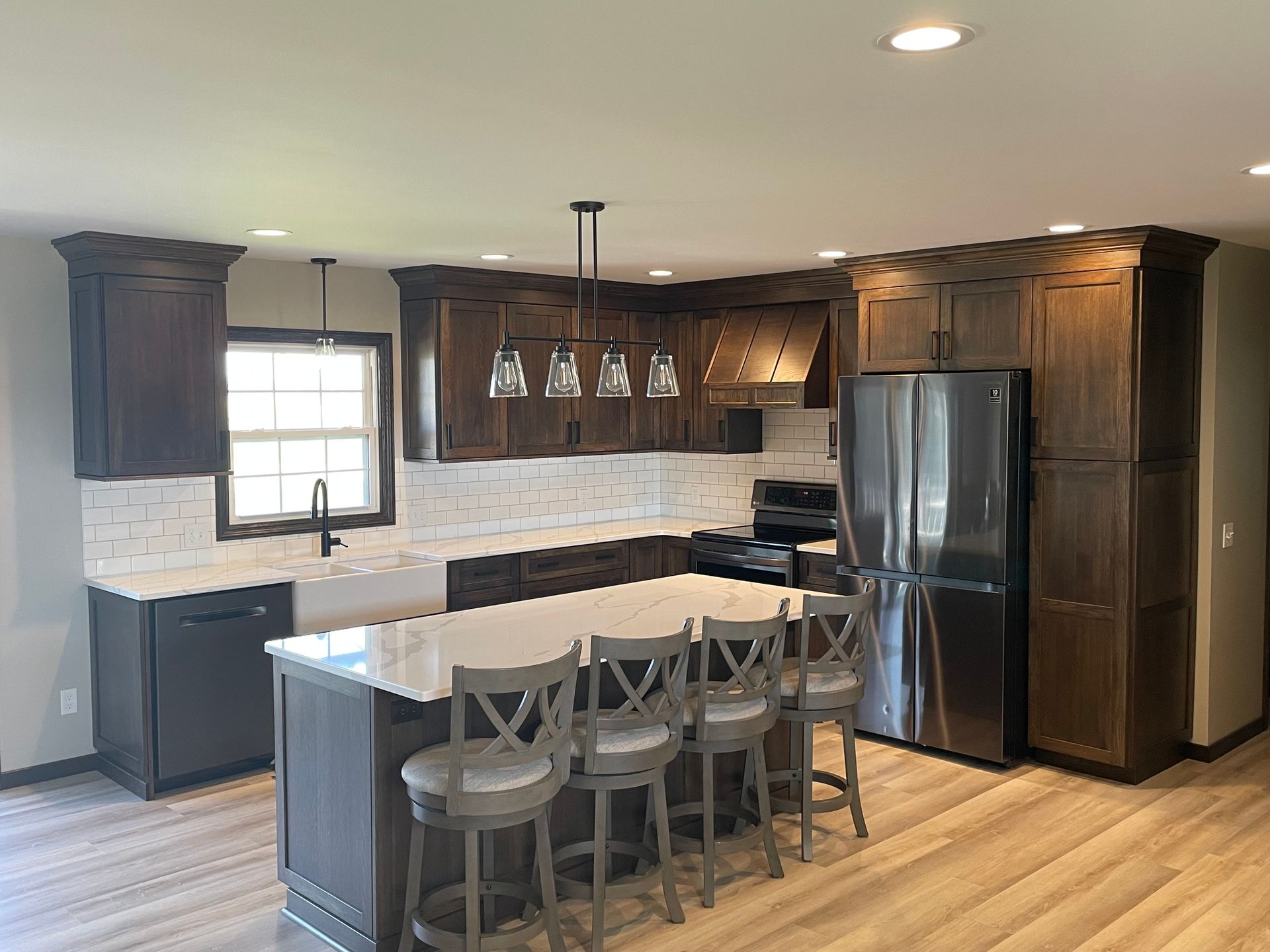 Modern kitchen with dark wood cabinets, white countertops, and an island with bar stools.