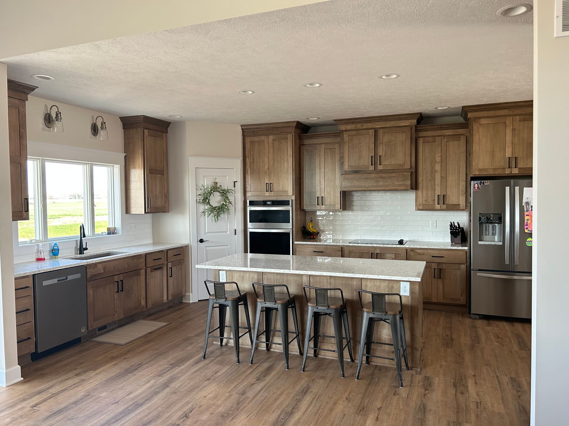 Spacious kitchen with wood cabinets, island with stools, stainless steel appliances, and white countertops.