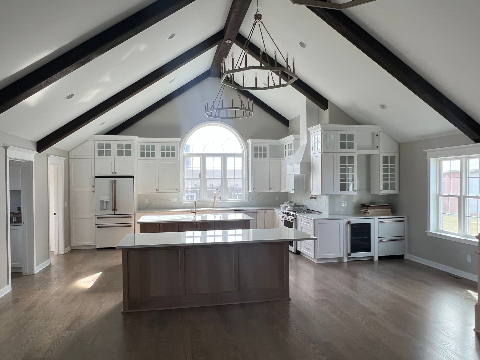 Spacious, white kitchen with dark wood beams, island, and large window.
