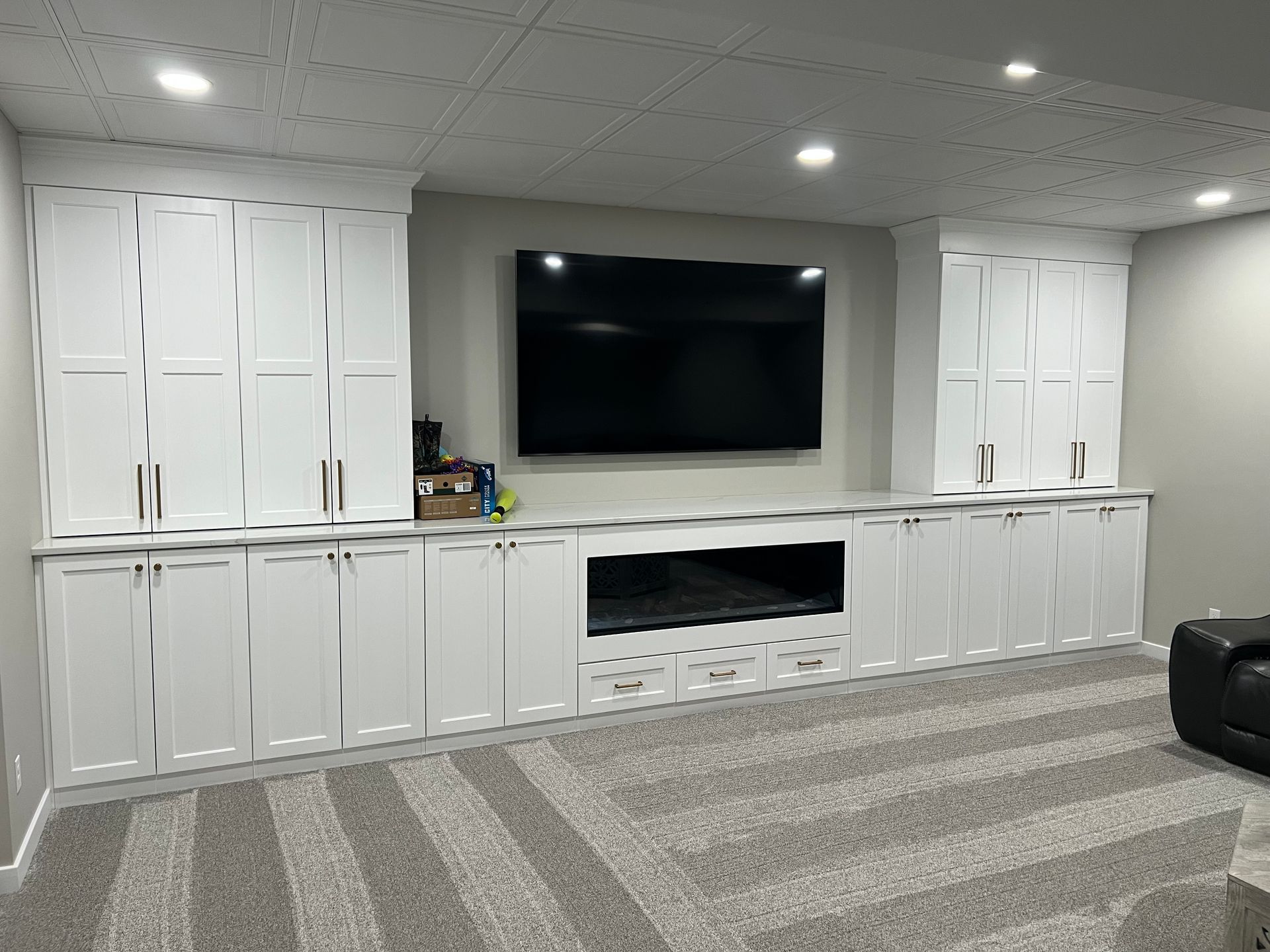 White built-in cabinets surround a TV in a room with gray carpet and a dropped ceiling.