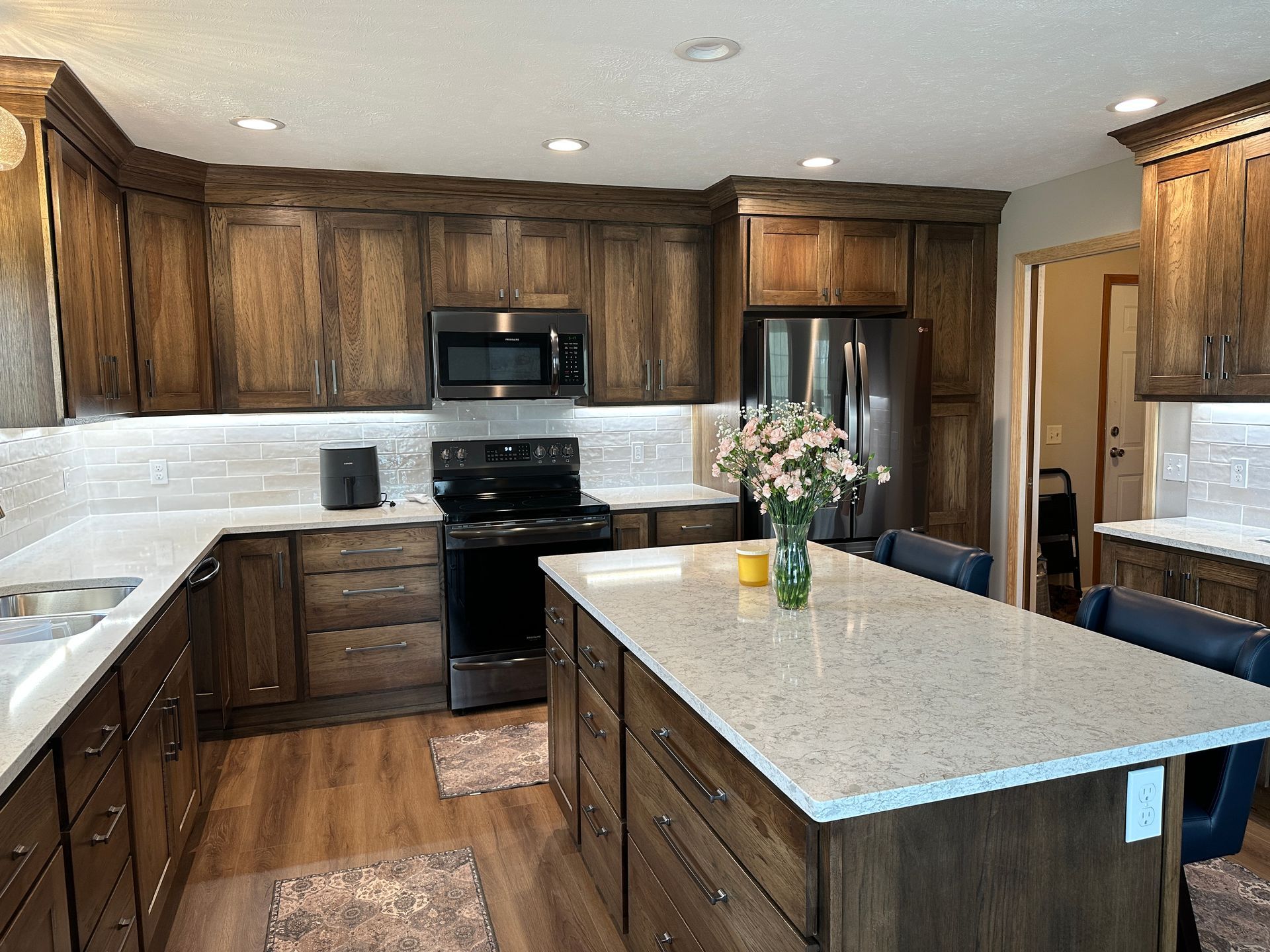 Modern kitchen with dark wood cabinets, black appliances, white countertops, and a center island with flowers
