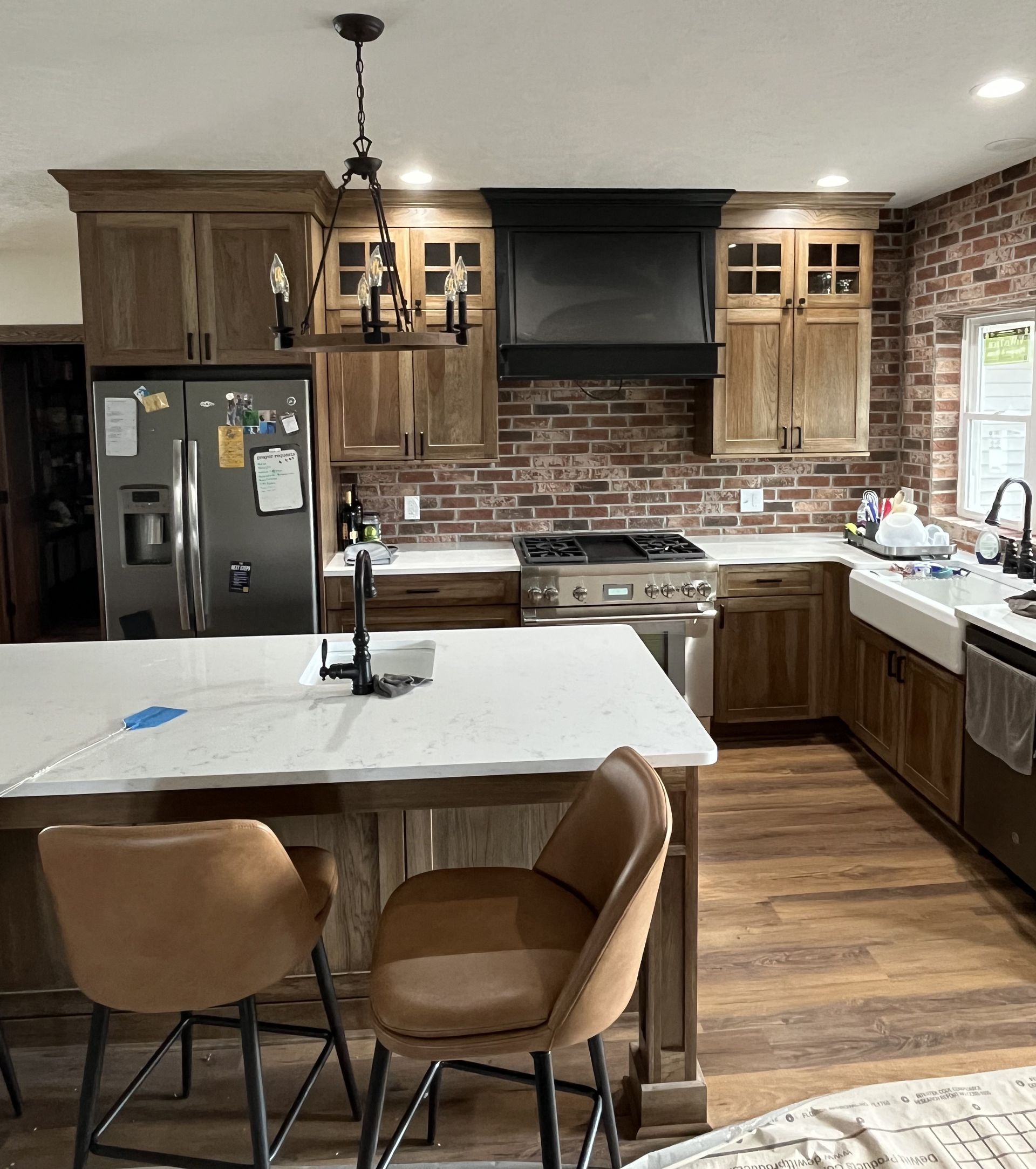 Kitchen with brick wall, wood cabinets, stainless steel appliances, and island with bar stools.