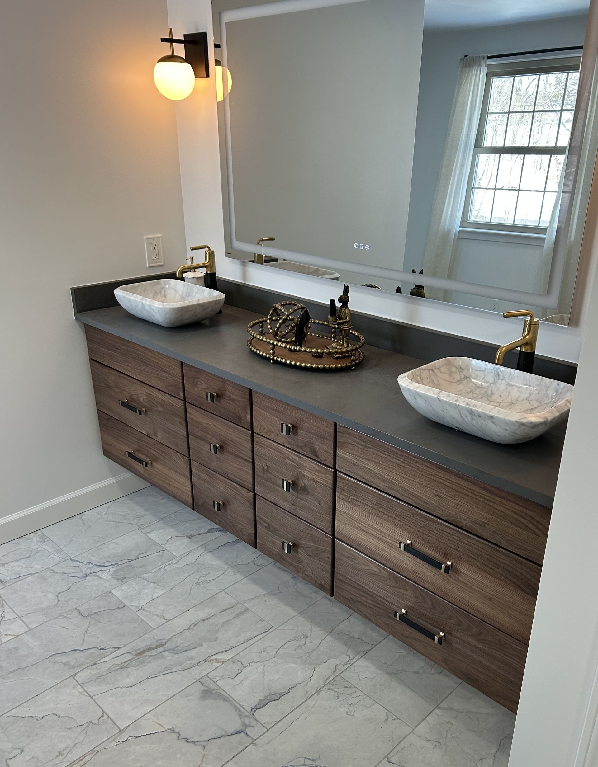 Floating vanity with two sinks, a large mirror, and dark brown drawers. Gold fixtures.